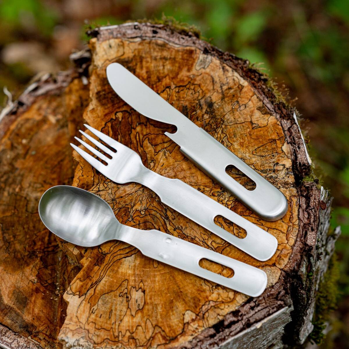 Tsubamesanjo Camp Cutlery SFK Set - elegant Japanese stainless steel fork, knife, and spoon displayed on a tree stump outdoors.