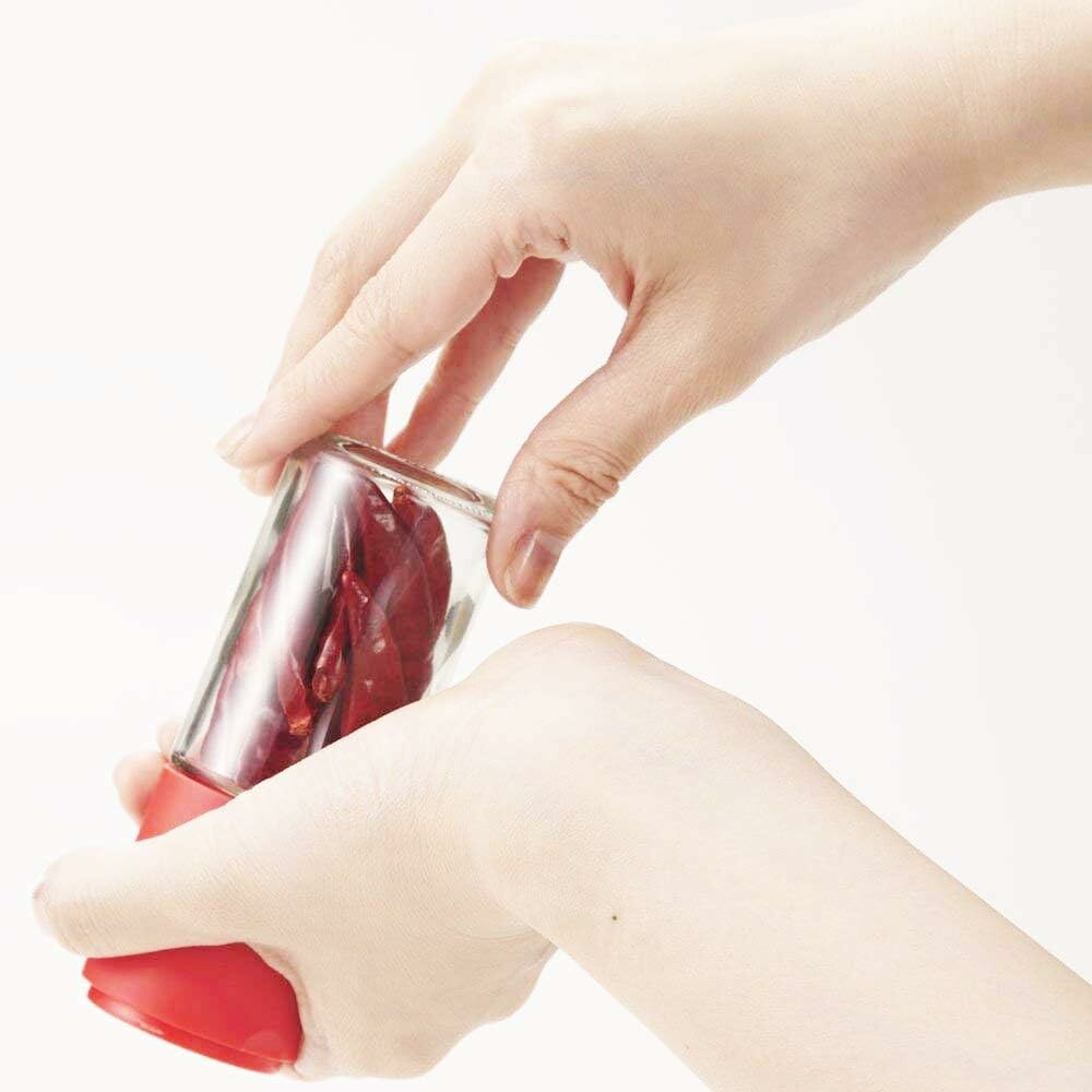 Hands using the Kai Home Pepper Mill - Ceramic Grinder, demonstrating ergonomic design and easy grinding of whole dried peppers.