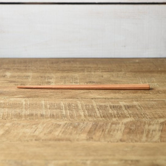 Single Kawai Tetoca Chopstick - Mandarine Wood laid flat on rustic wood table, emphasizing its tapered tip and natural ergonomic form.