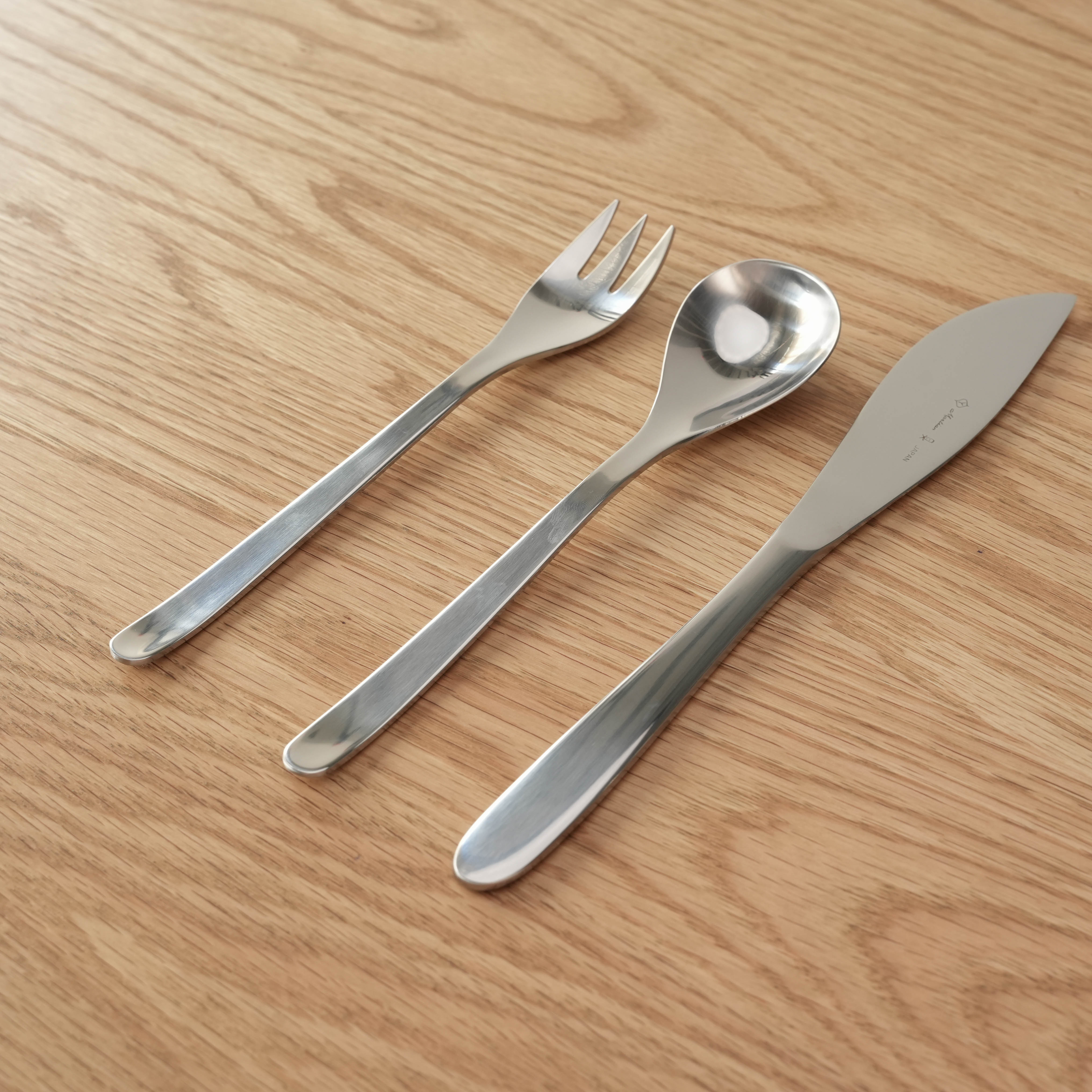 Sori Yanagi Stainless Steel Table Cutlery 3 Piece Set with spoon, fork, and knife on wooden surface. Sleek modern design for stylish dining.