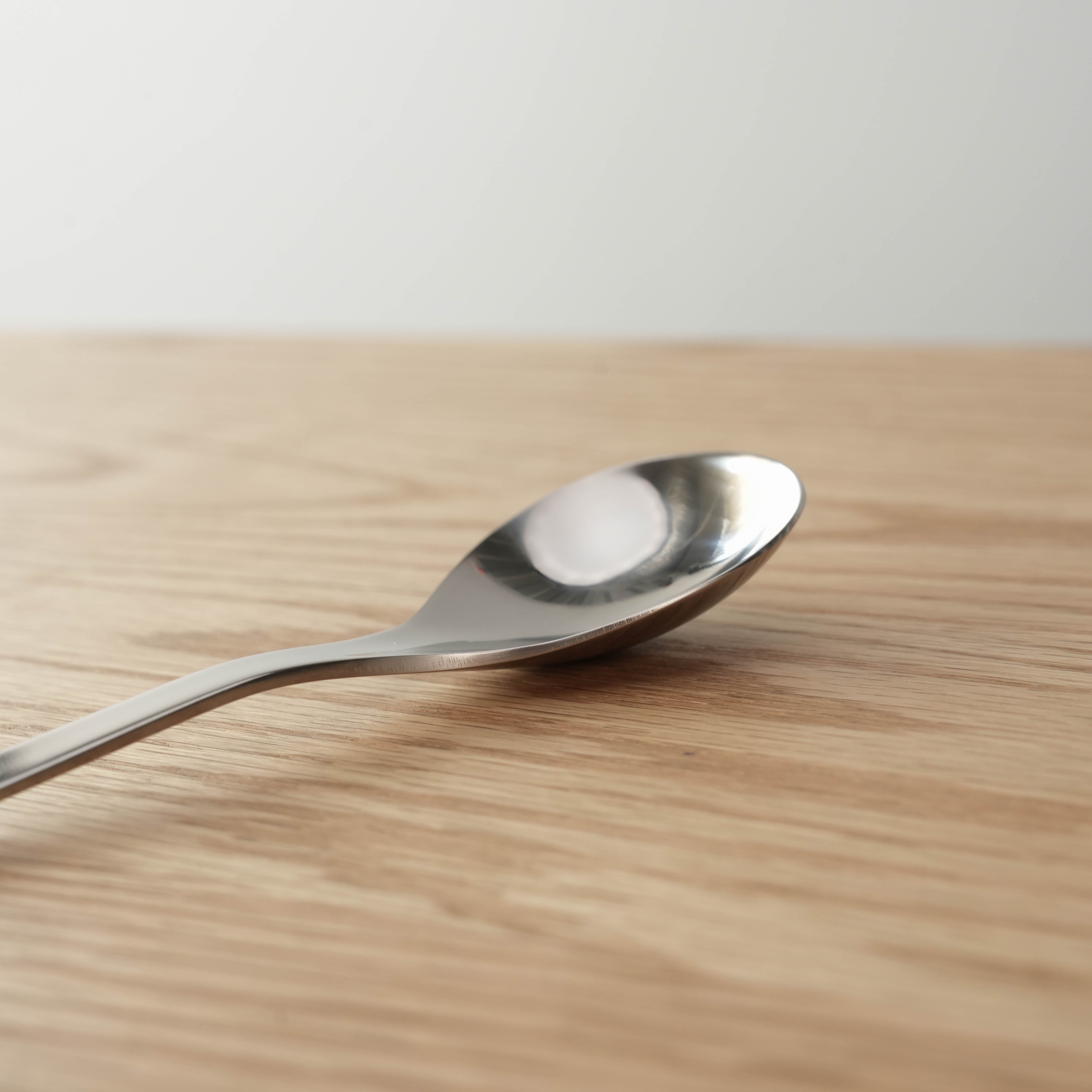 Close-up of Sori Yanagi stainless steel dessert spoon showcasing its smooth, reflective bowl and ergonomic design.