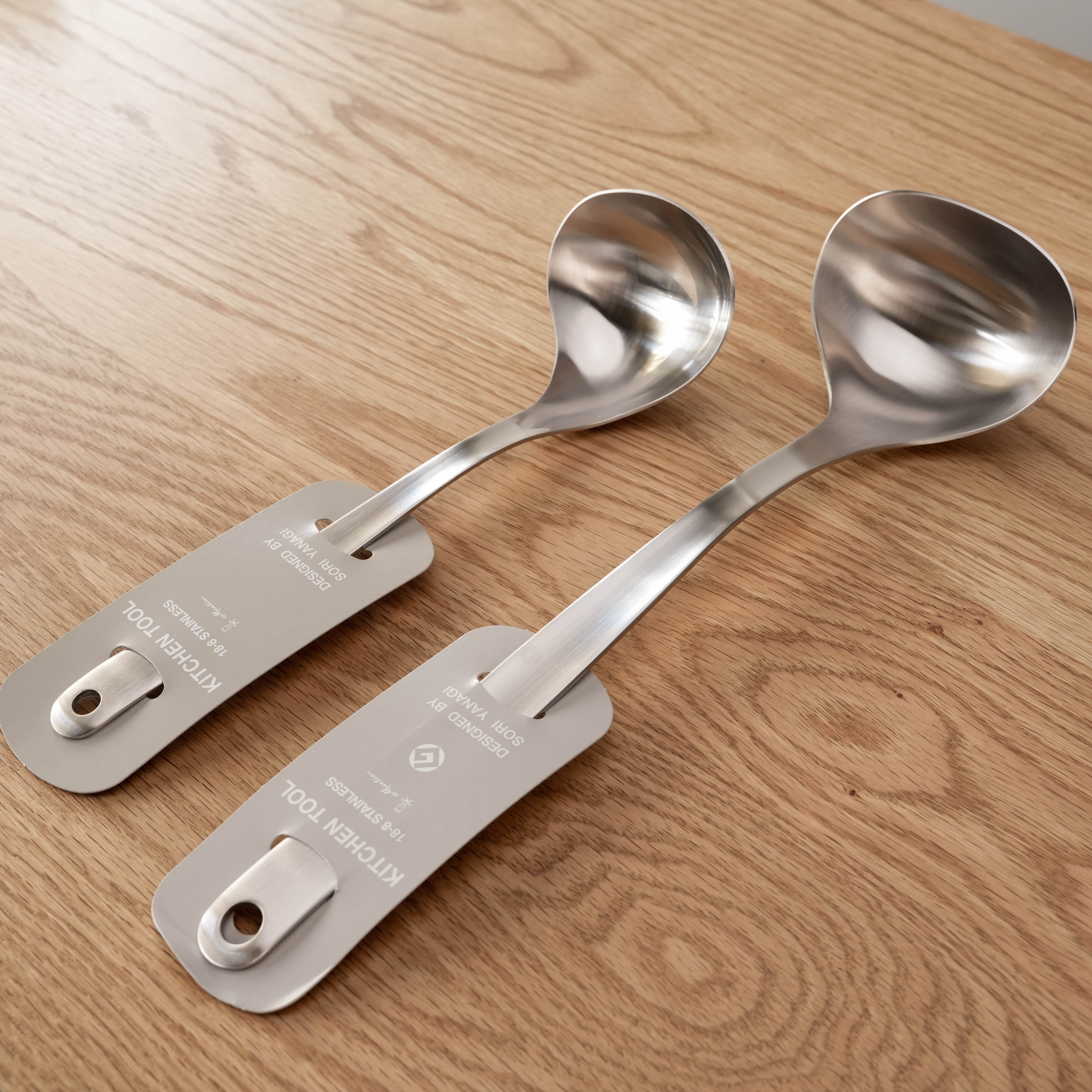 Small and medium Sori Yanagi stainless steel ladles with sleek design, ideal for modern kitchens, displayed on a wooden countertop.