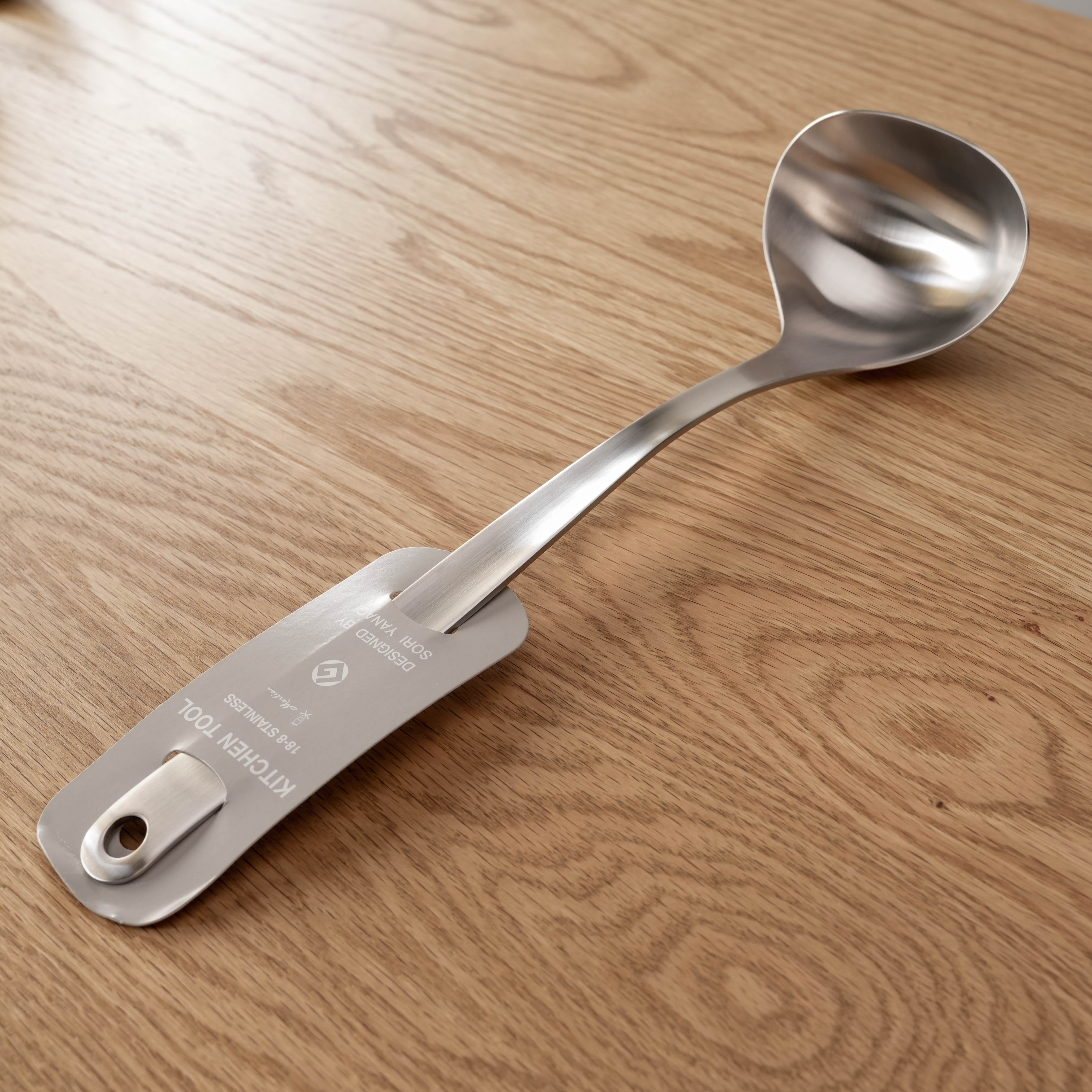 Sori Yanagi Ladle - Stainless Steel | Dishwasher Safe, shown on a wooden surface with ergonomic curved handle and brushed finish.