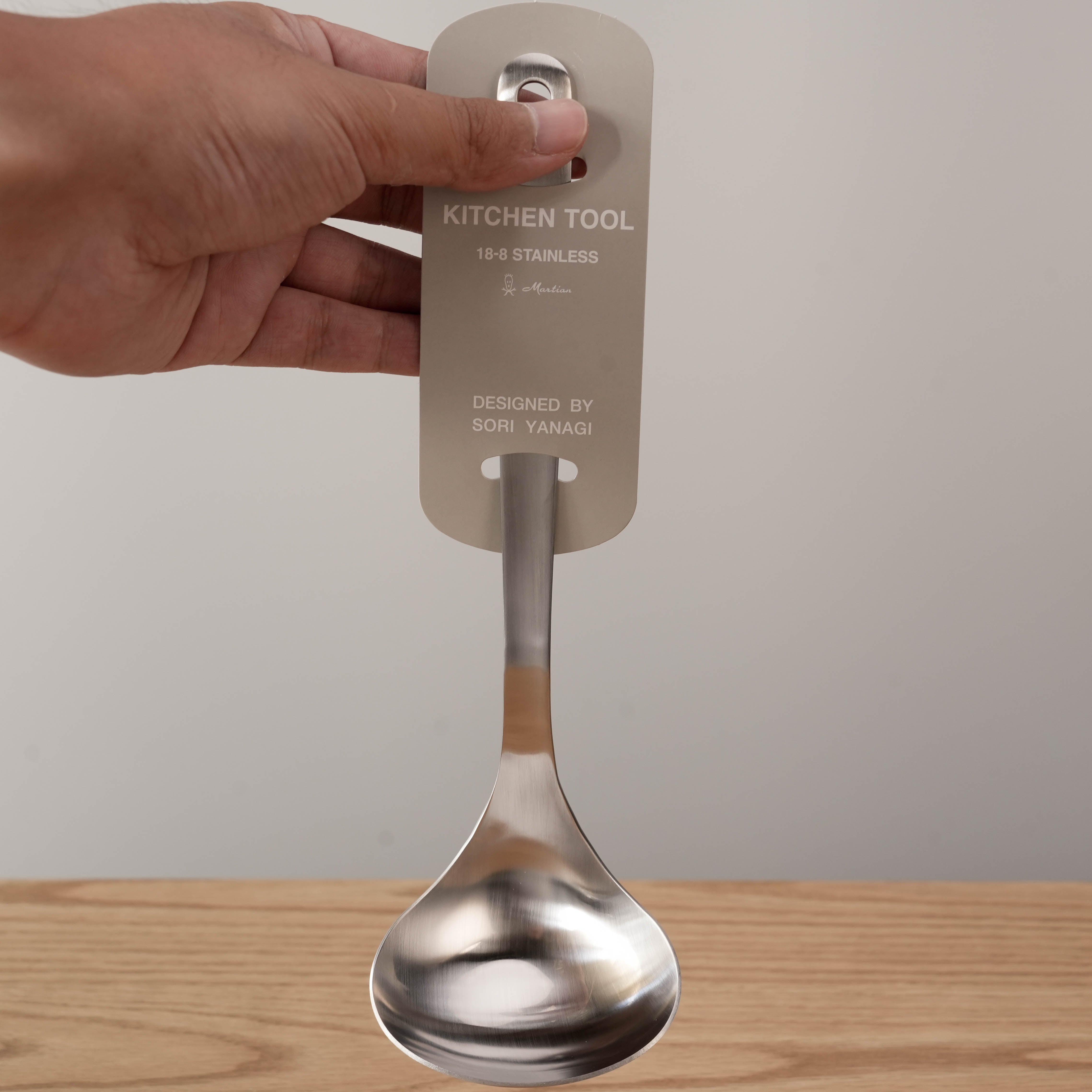 Sori Yanagi stainless steel ladle held by hand, featuring ergonomic handle and product tag, perfect for daily kitchen use.