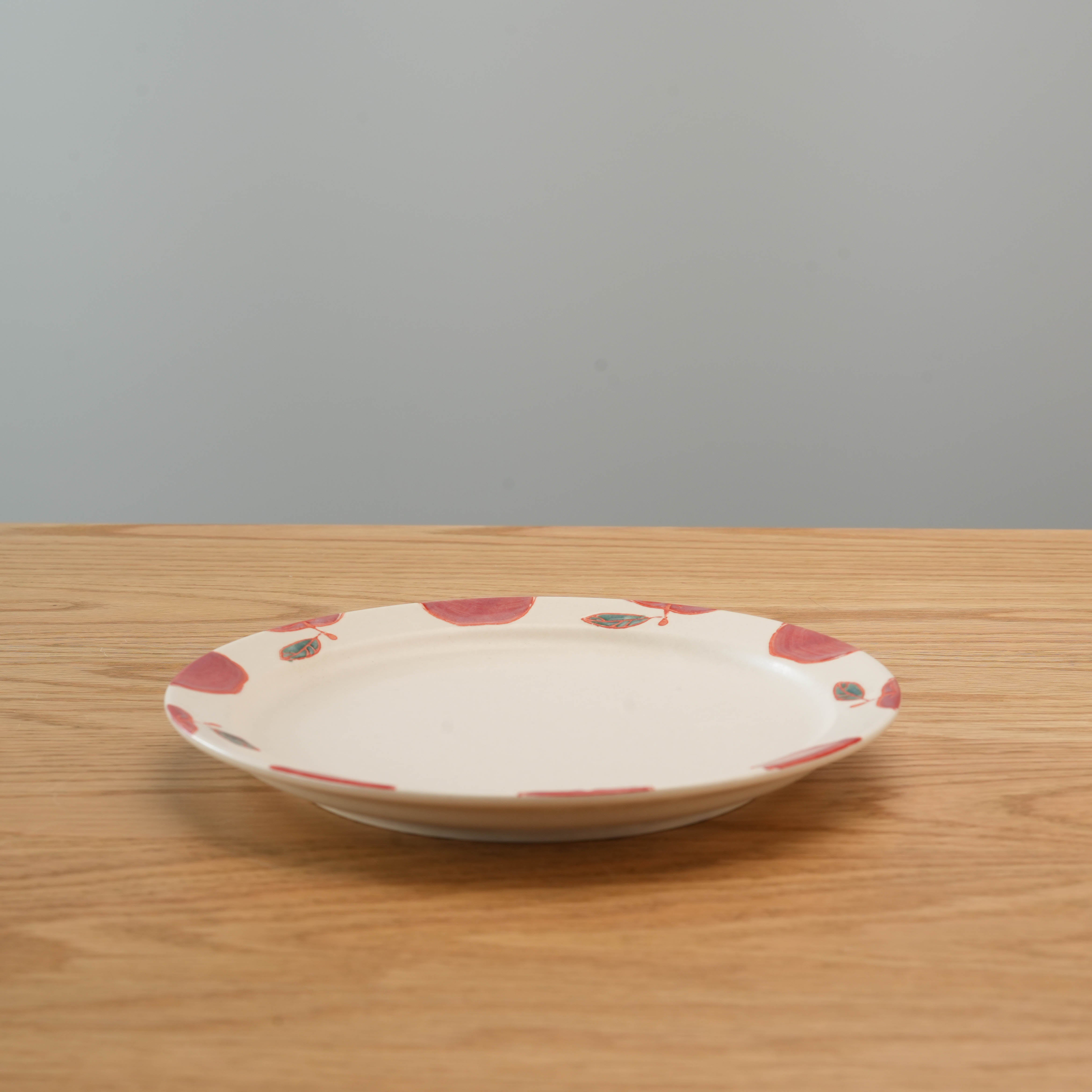Side view of Hasami Ware Apple Plate on wooden table, highlighting its smooth ceramic finish and unique apple pattern for elegant table settings.