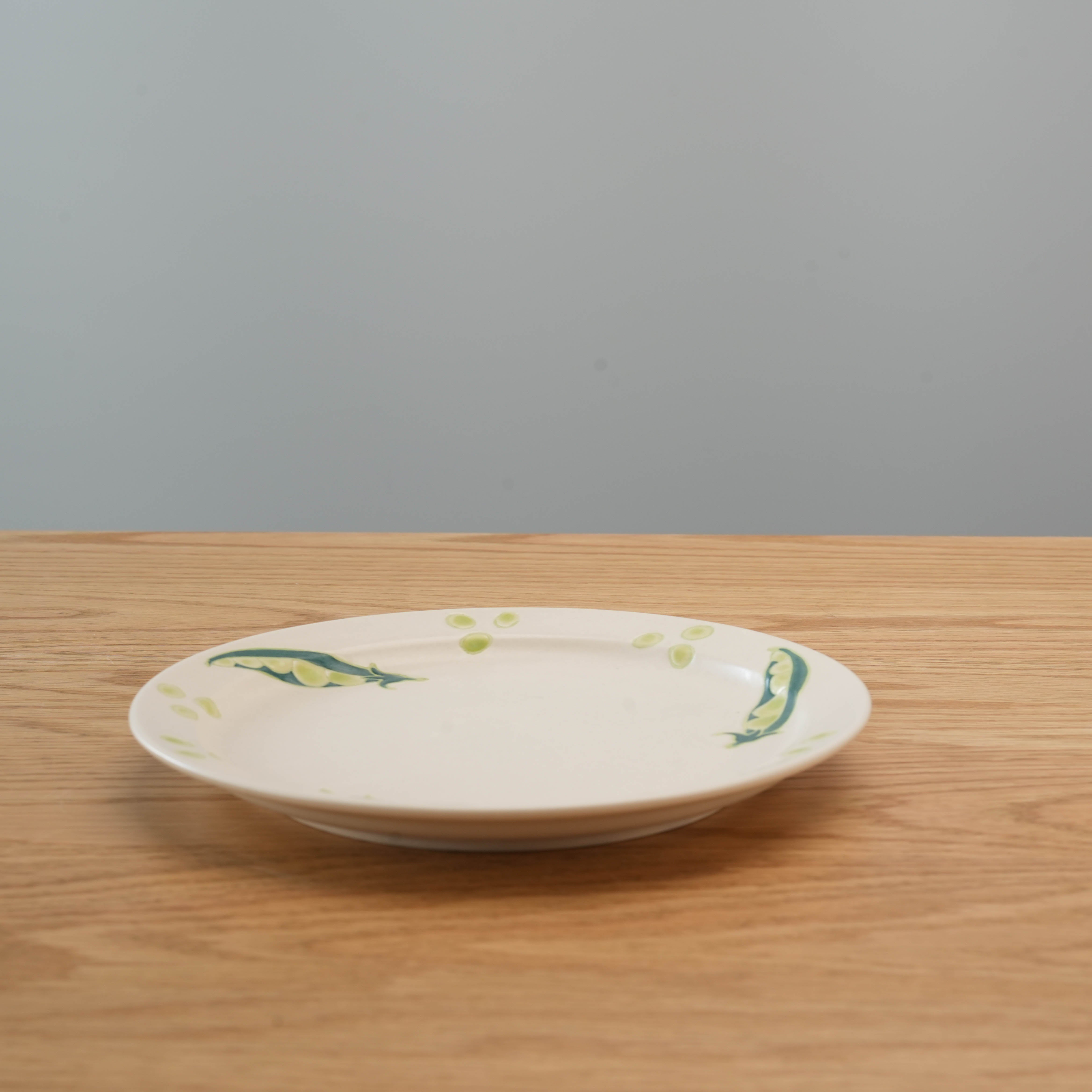Side view of Hasami Round Plate - Veggie Art featuring green pea illustrations, showcasing its shallow depth and smooth ceramic finish.