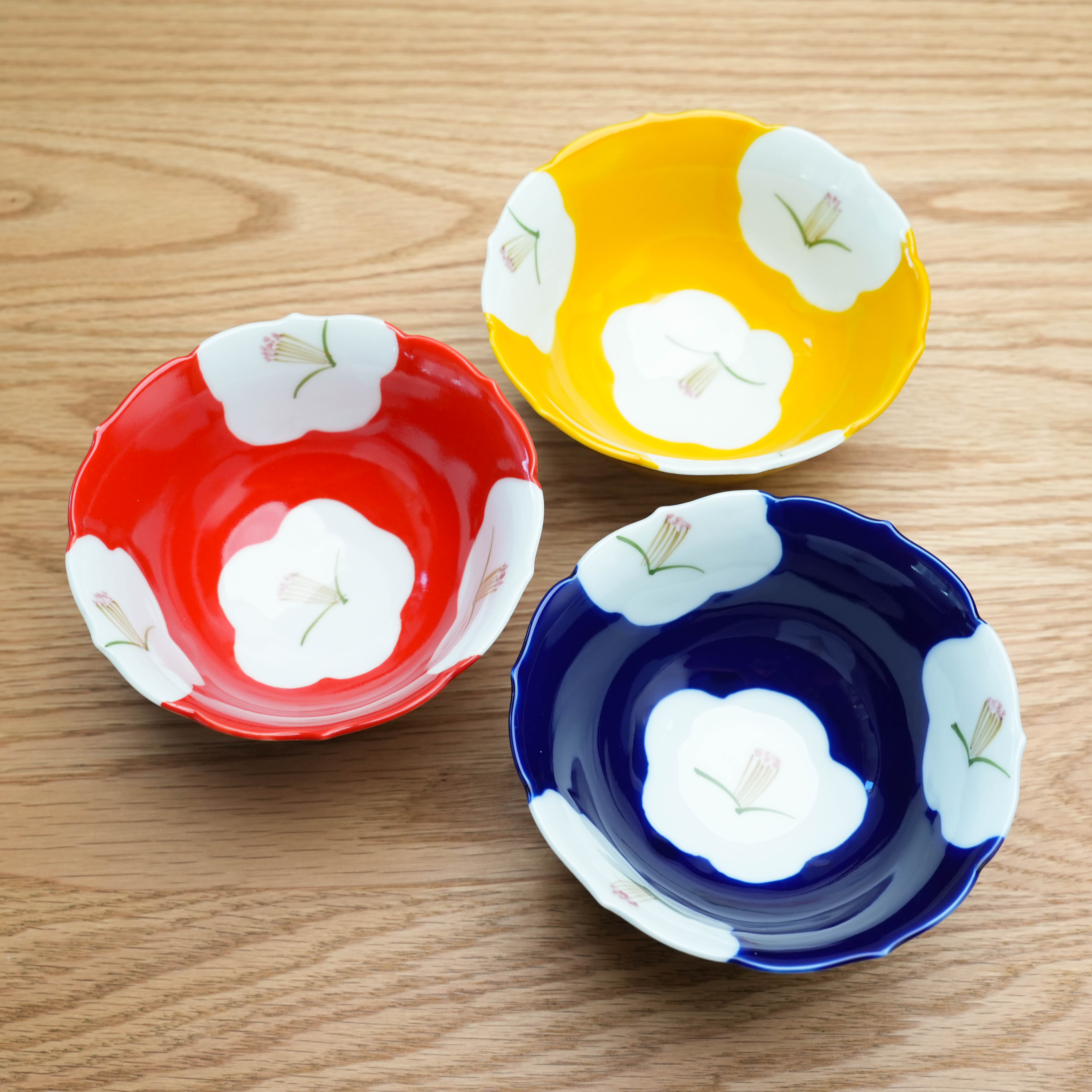 Set of three Arita Ware Plum Blossom Petal Rim Bowls in red, yellow, and navy with floral motifs, ideal for elegant Japanese-style dining.