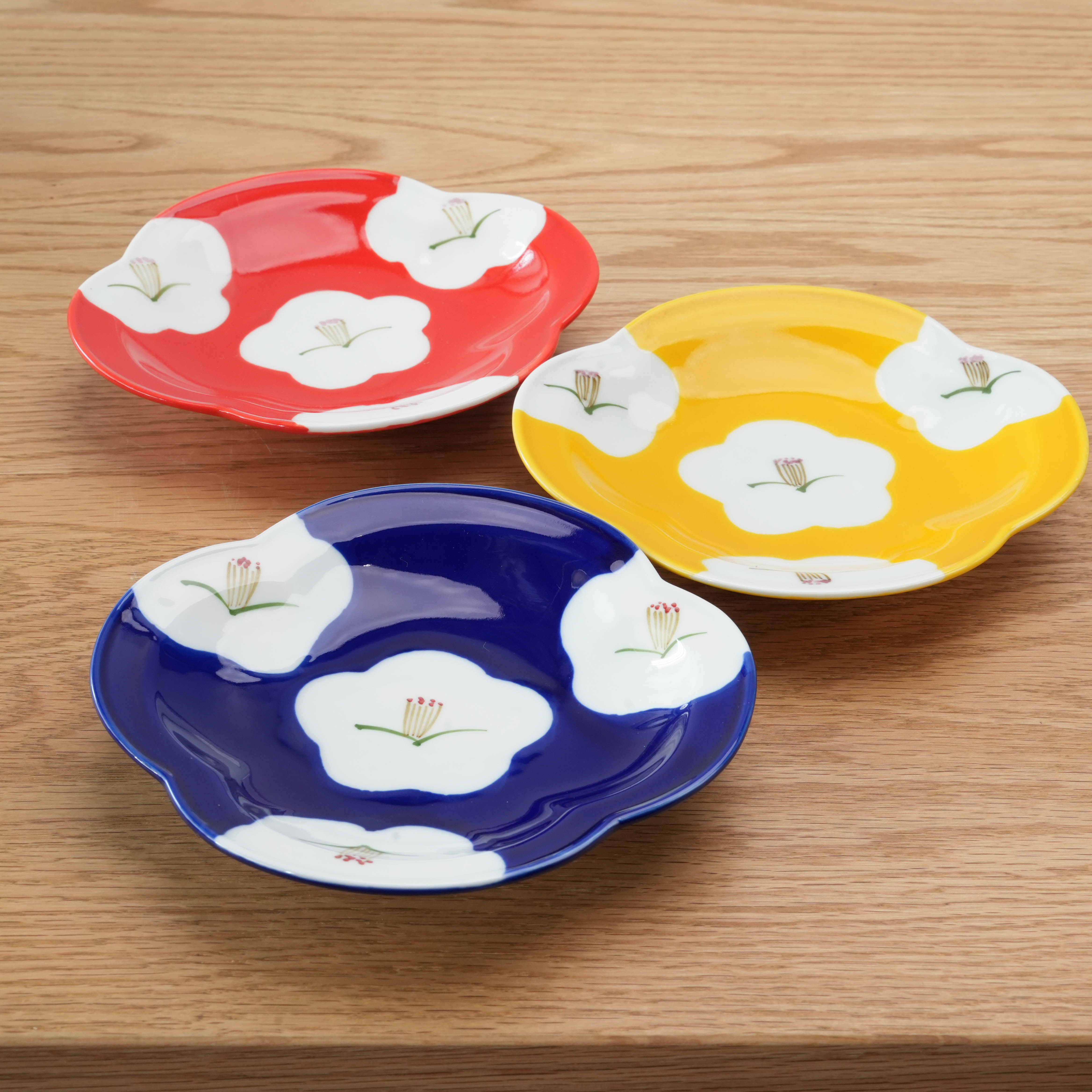 Set of three Arita Ware Plum Blossom Plates in red, yellow, and lapis lazuli blue with white floral design, ideal for elegant Japanese table settings.
