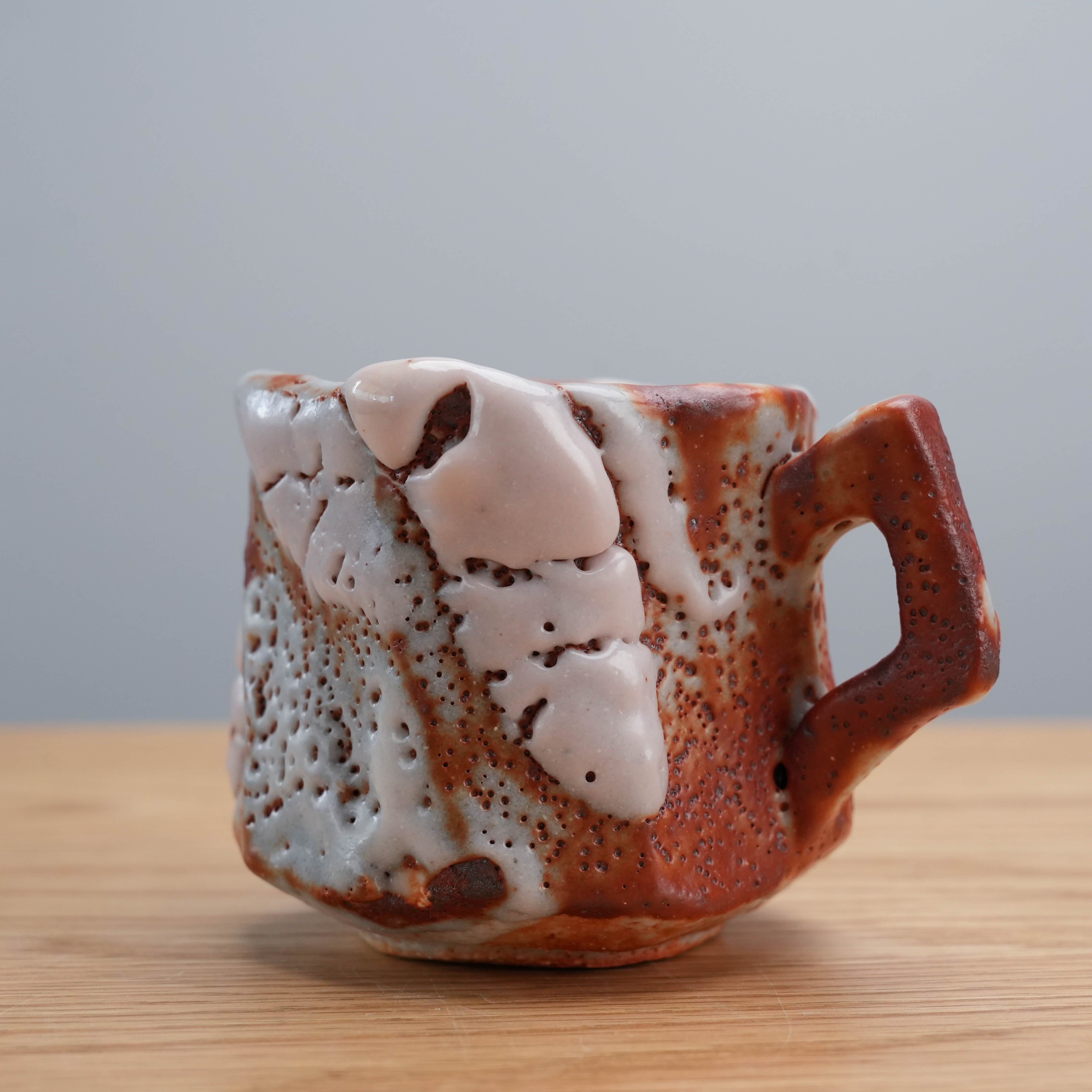 Angled view of Kano Shinji's red Shino ceramic cup, emphasizing the sculptural form and expressive glaze technique.