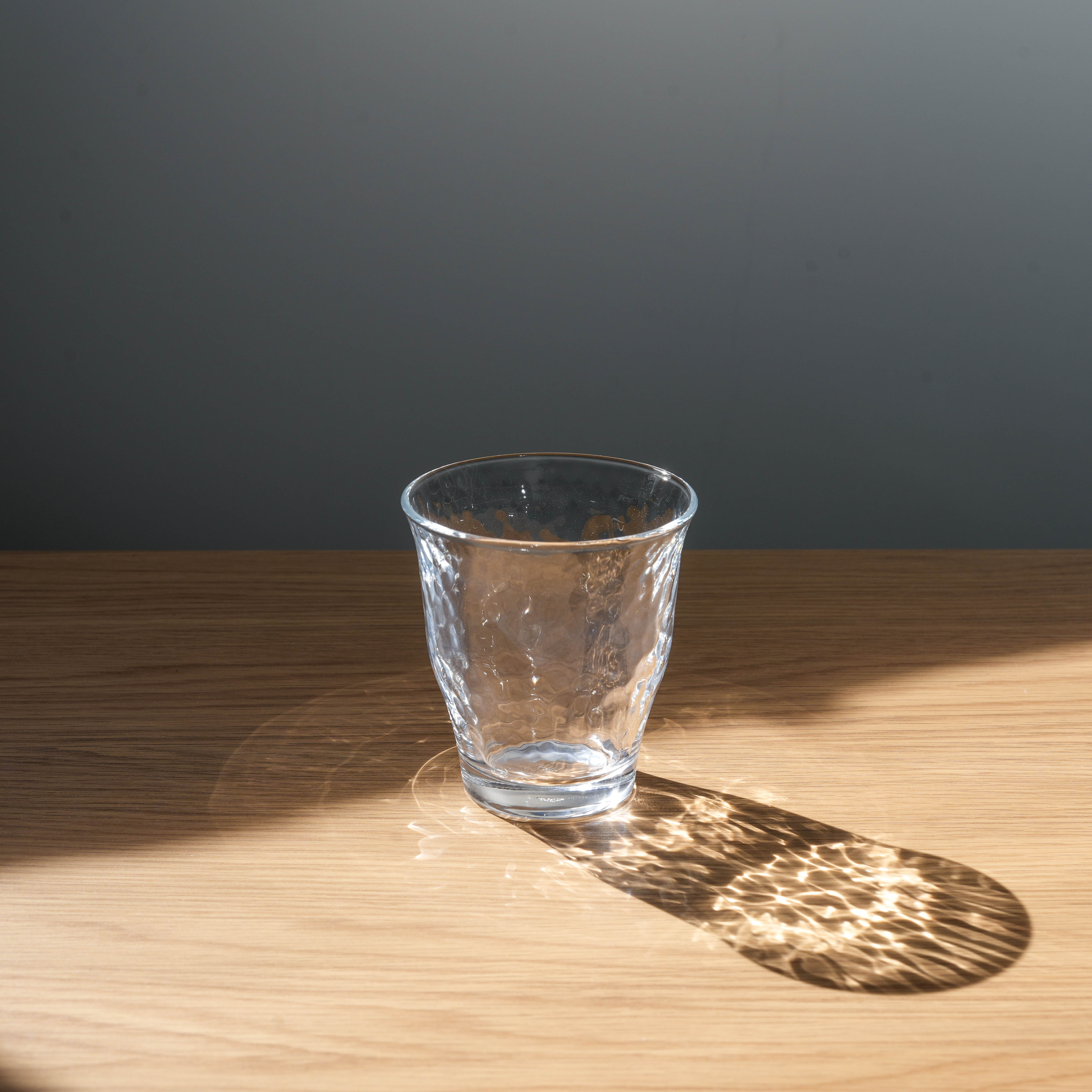 Irodori Seikatsu Glasses - Japanese Glass Cup with hammered texture, reflecting light on wooden surface. Elegant drinkware for modern kitchens.