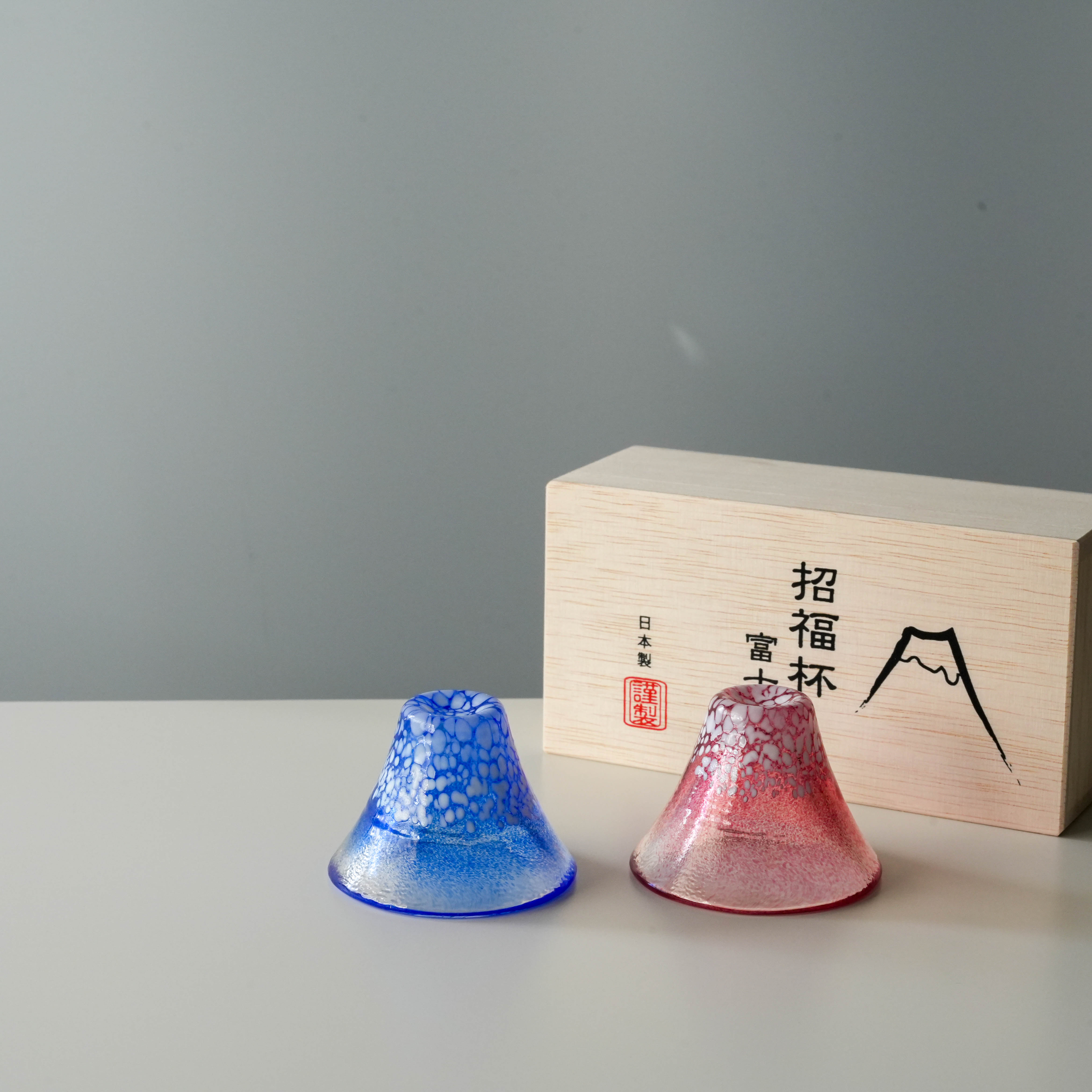 Mt. Fuji-inspired sake cups in red and blue glass from the Fuji Sake Cup Set - Handmade Japan, shown with wooden presentation box.