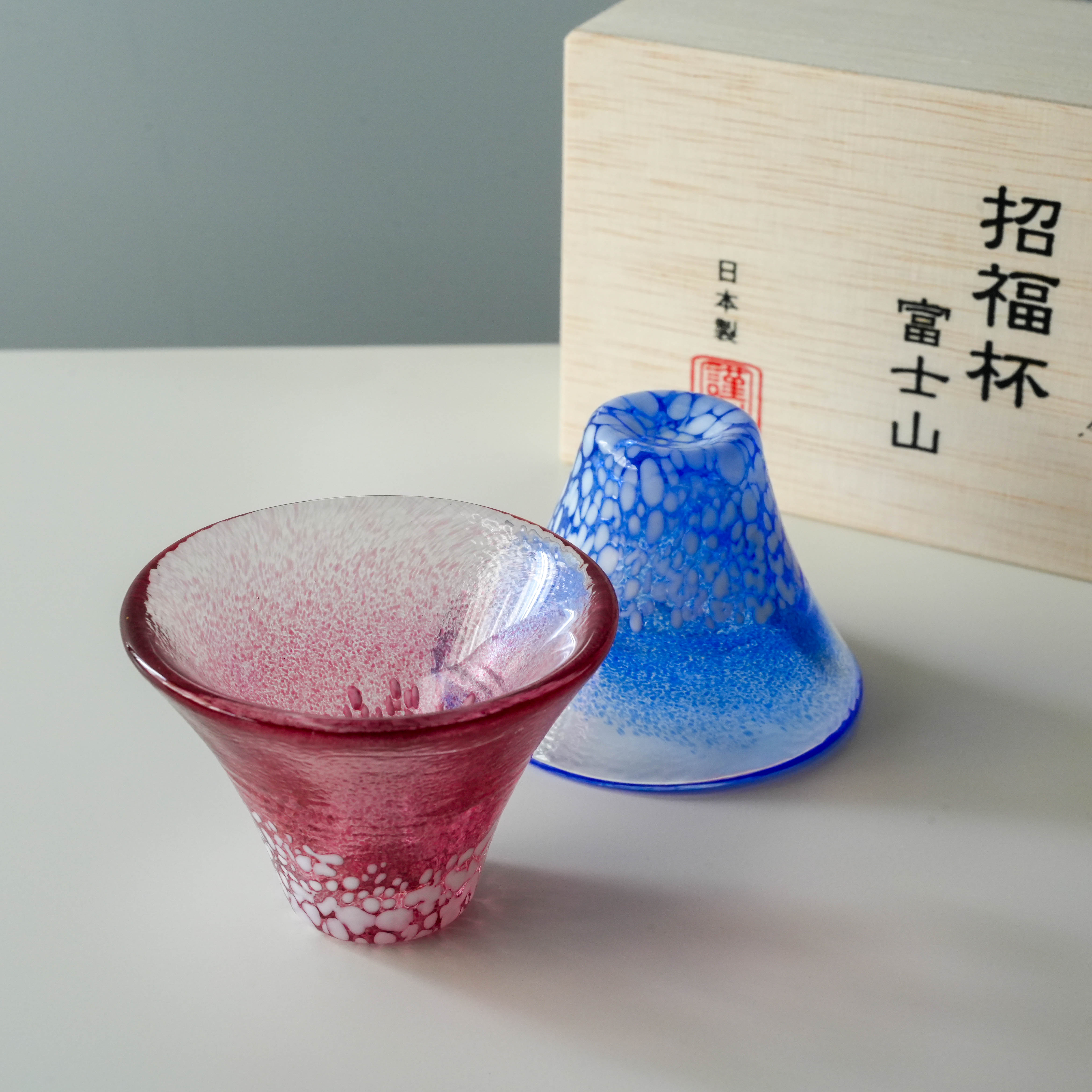 Close-up of Fuji Sake Cup Set - Handmade Japan, showing red and blue Mt. Fuji-shaped cups with textured glass and wooden box packaging.