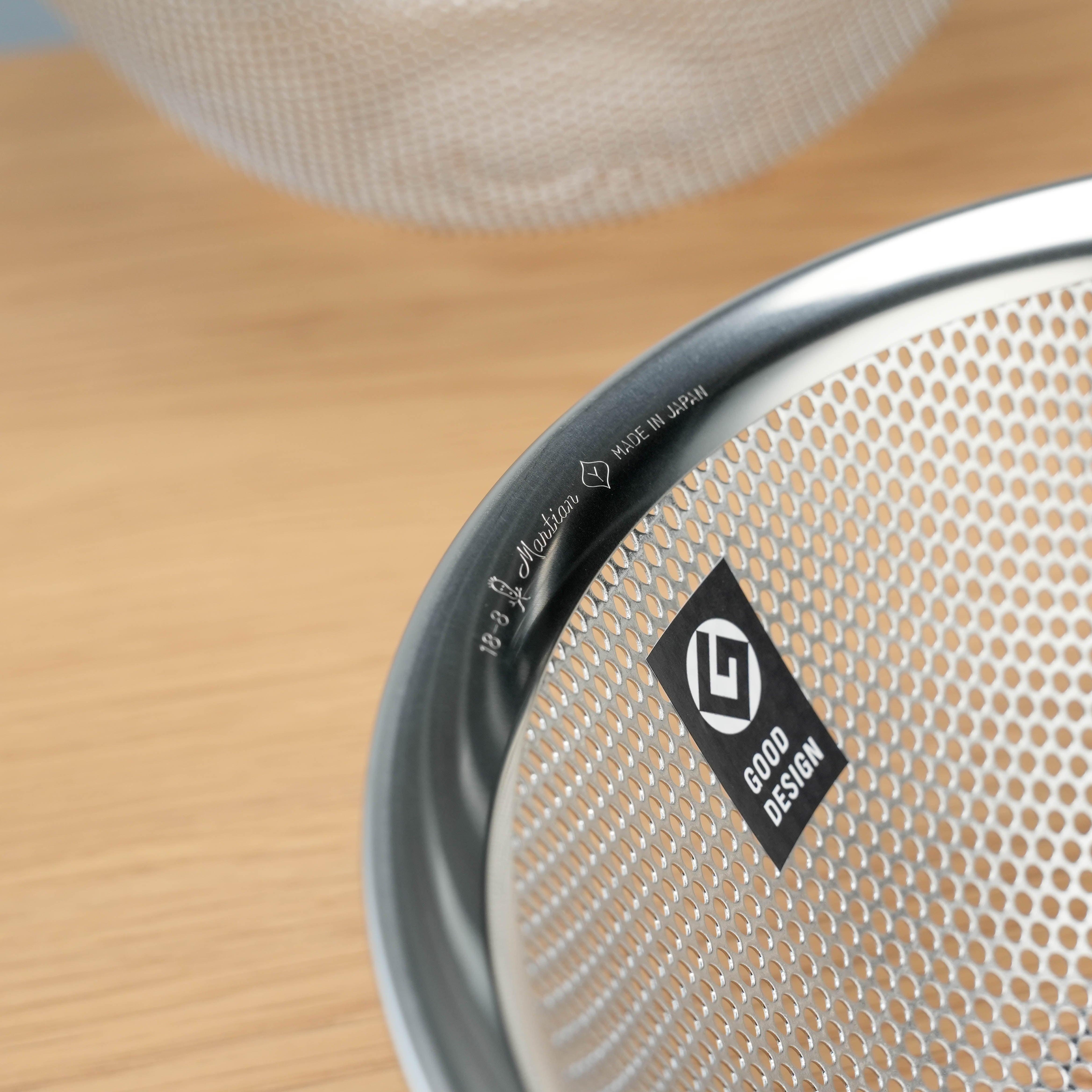 Close-up of Sori Yanagi Stainless Steel Perforated Colander featuring Good Design award label and precision Japanese craftsmanship.