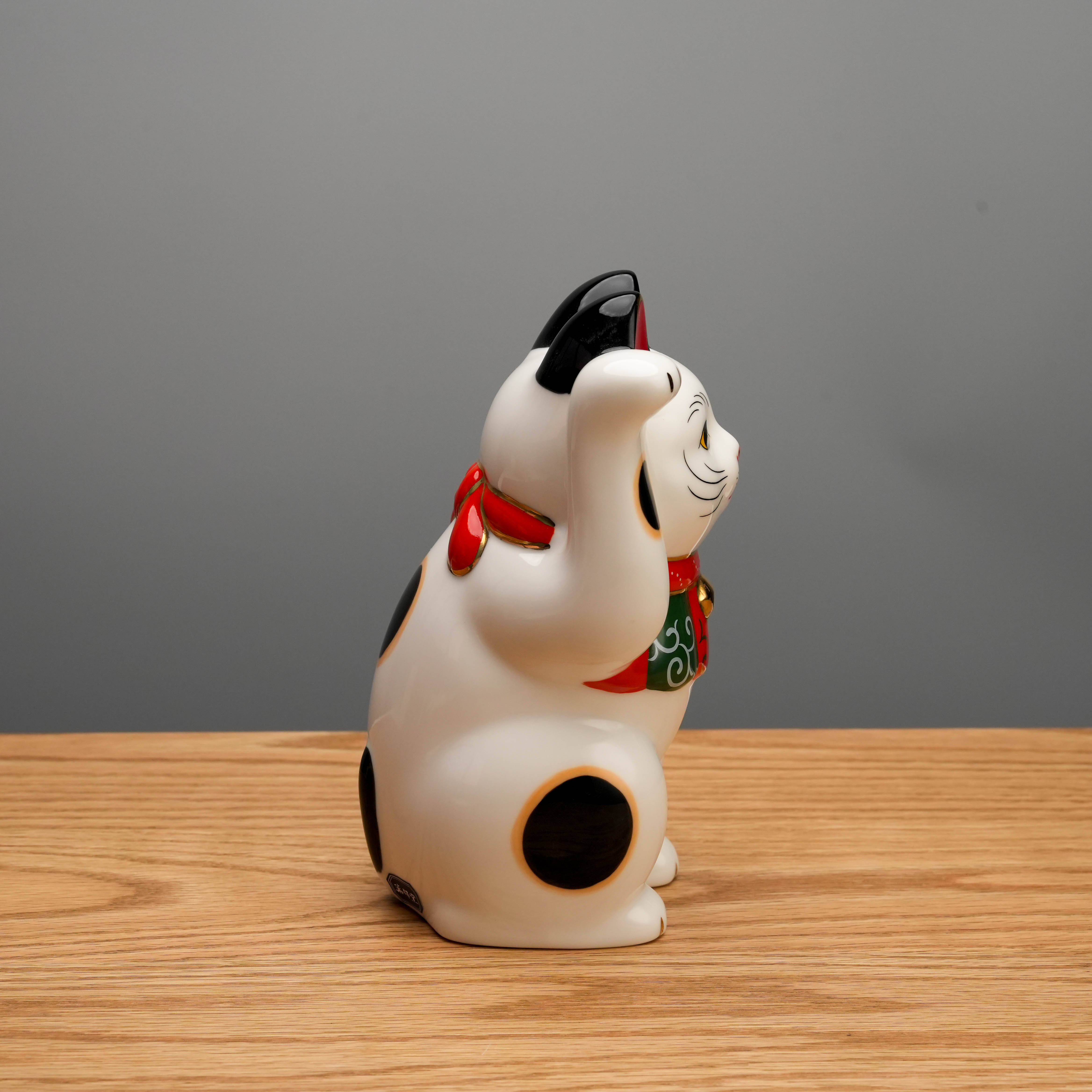 Side view of Yakushigama Arabesque Scarf Beckoning Cat highlighting black spots and red bow, a lucky charm for home or office decor.