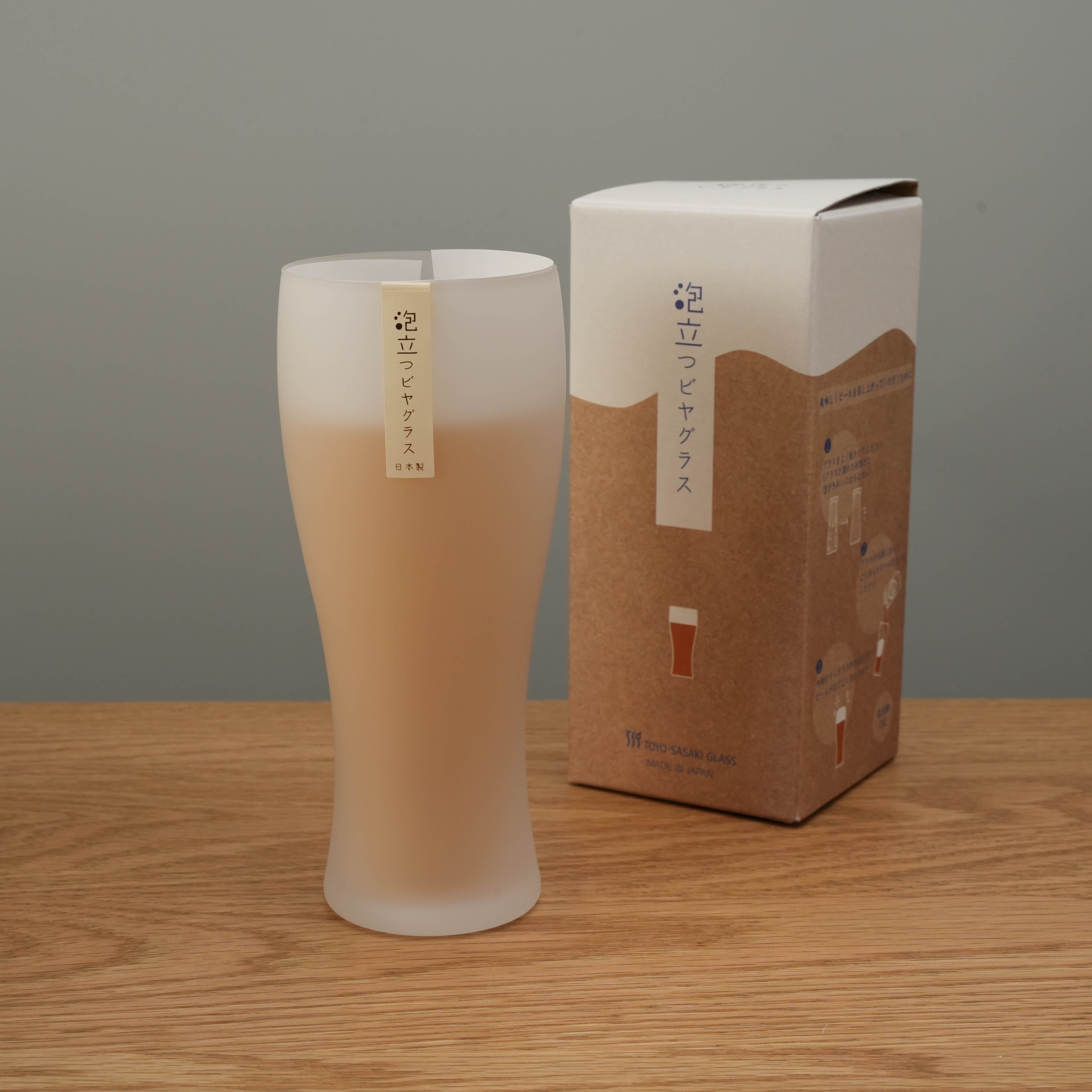 Toyo-Sasaki Frosted Glass Schooner Beer Glass filled with beer, displayed next to its original packaging. Perfect for premium beer presentation at home.