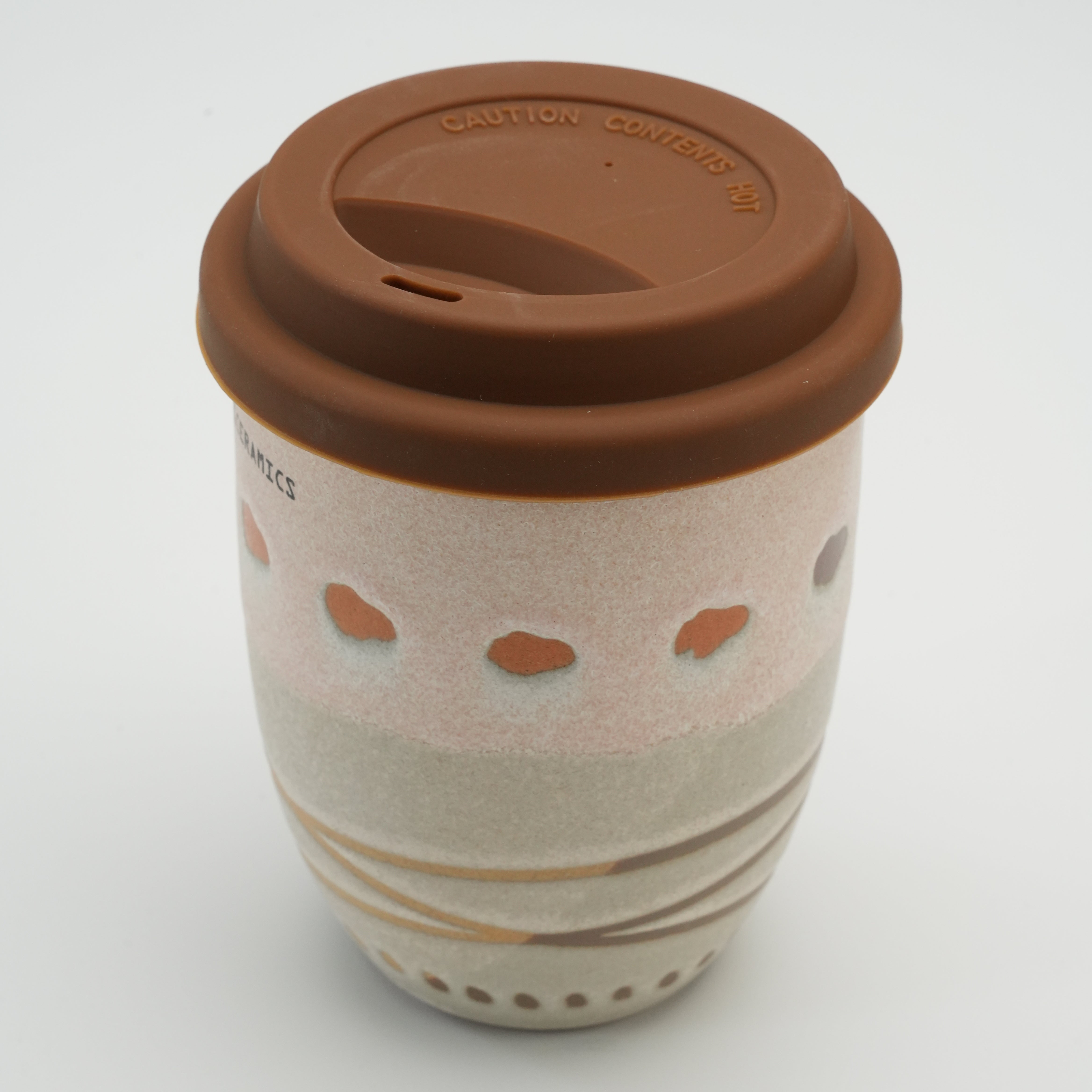 Angled top view of tall Handiceramics Travel Cup in Latte with brown silicone lid and handcrafted ceramic detailing for stylish coffee drinking.