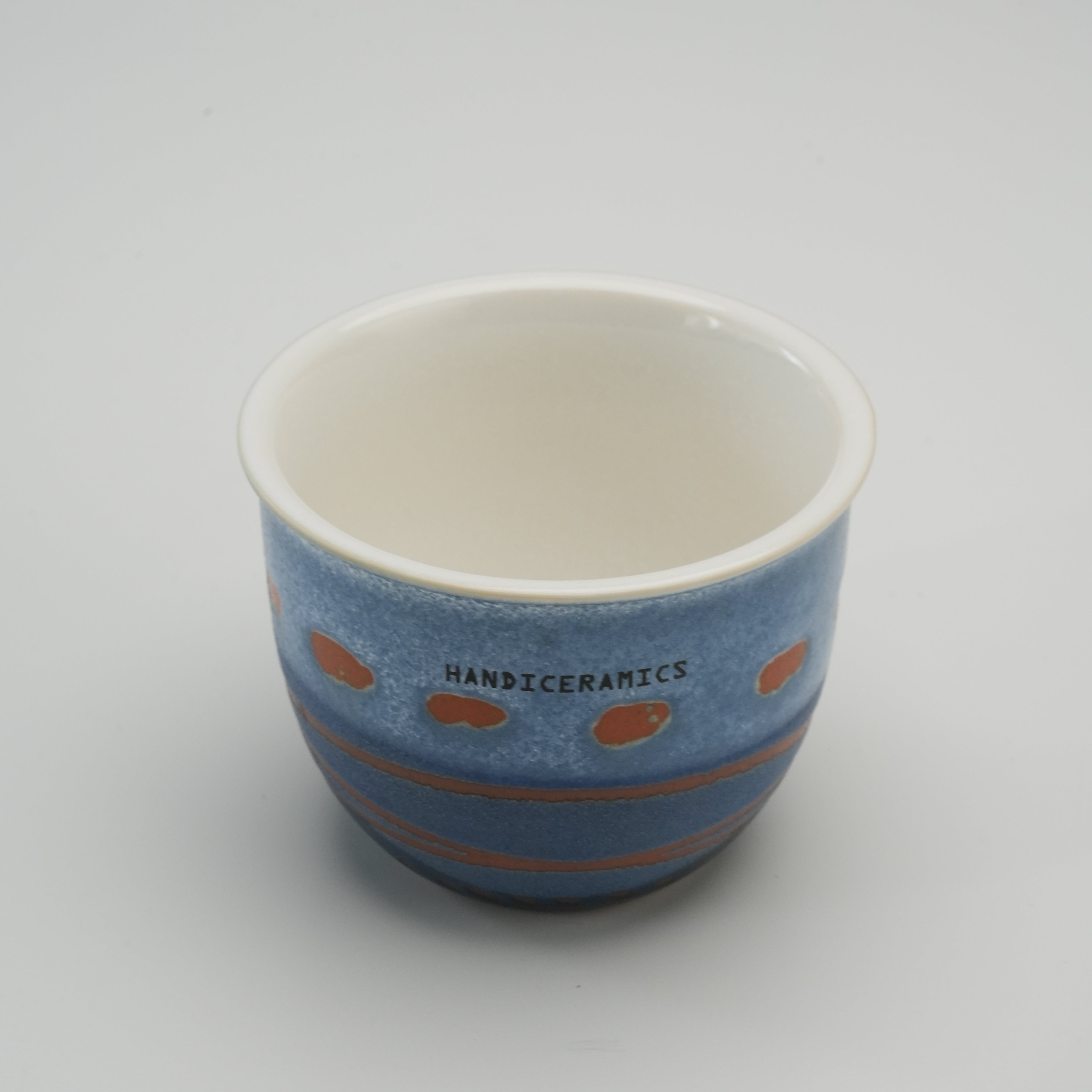 Interior view of the Handiceramics Acorn Travel Cup in Marine, showing smooth white porcelain finish and artisan exterior pattern.