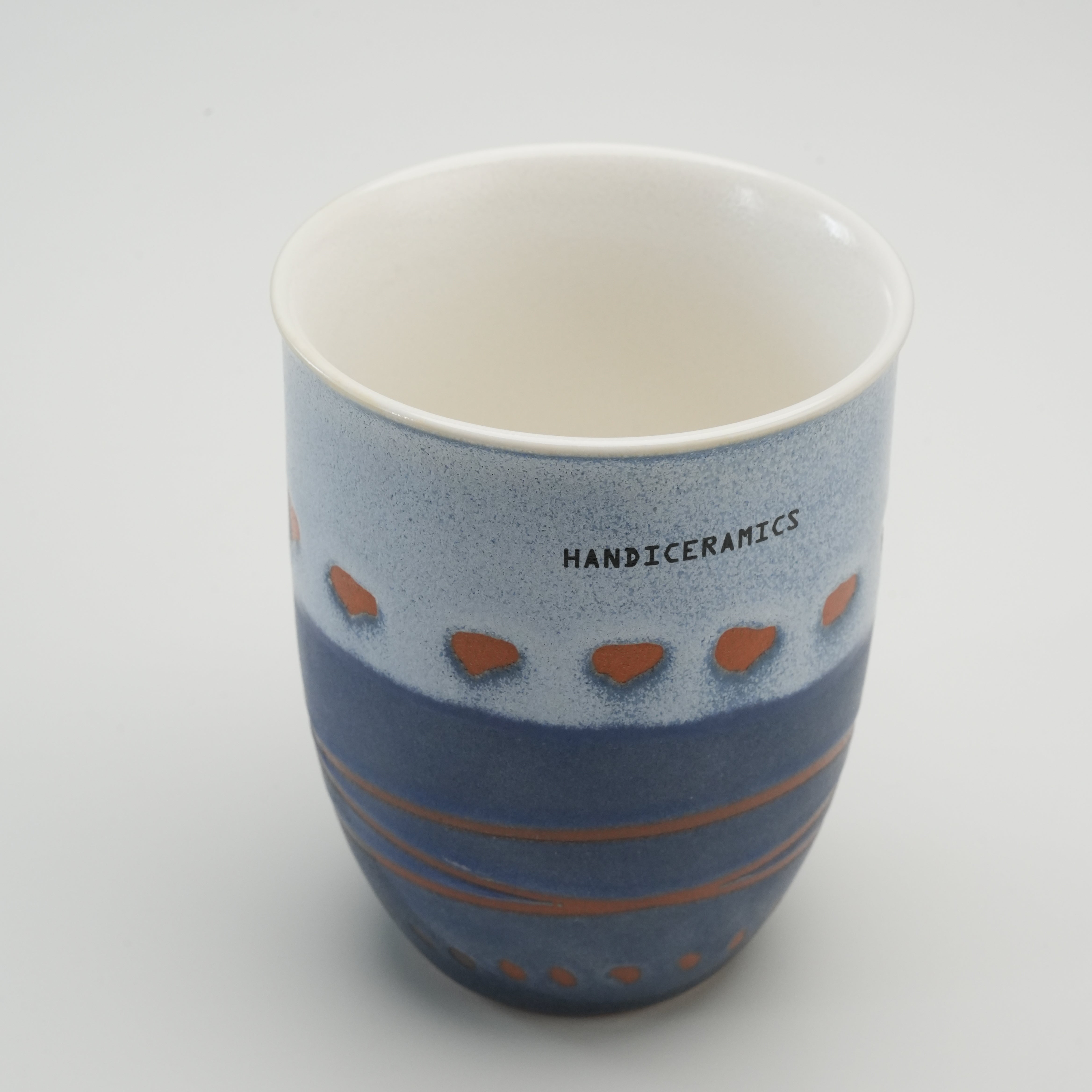 Open view of Handiceramics Marine ceramic travel cup, showing glossy white interior and blue-orange artisan exterior design.