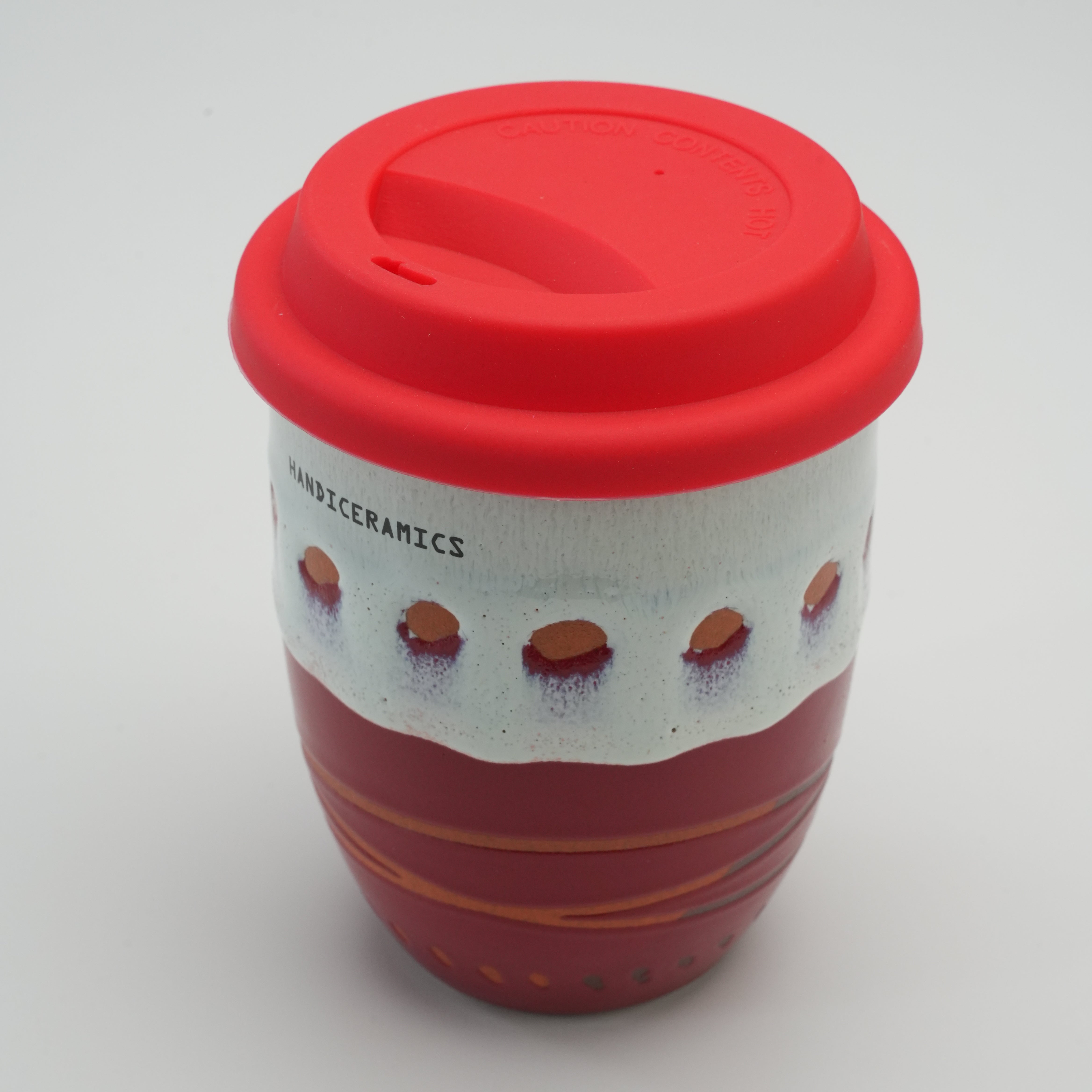 Top angle of the Handiceramics Travel Cup with red lid, emphasizing the secure fit and unique ceramic craftsmanship in a raspberry color scheme.