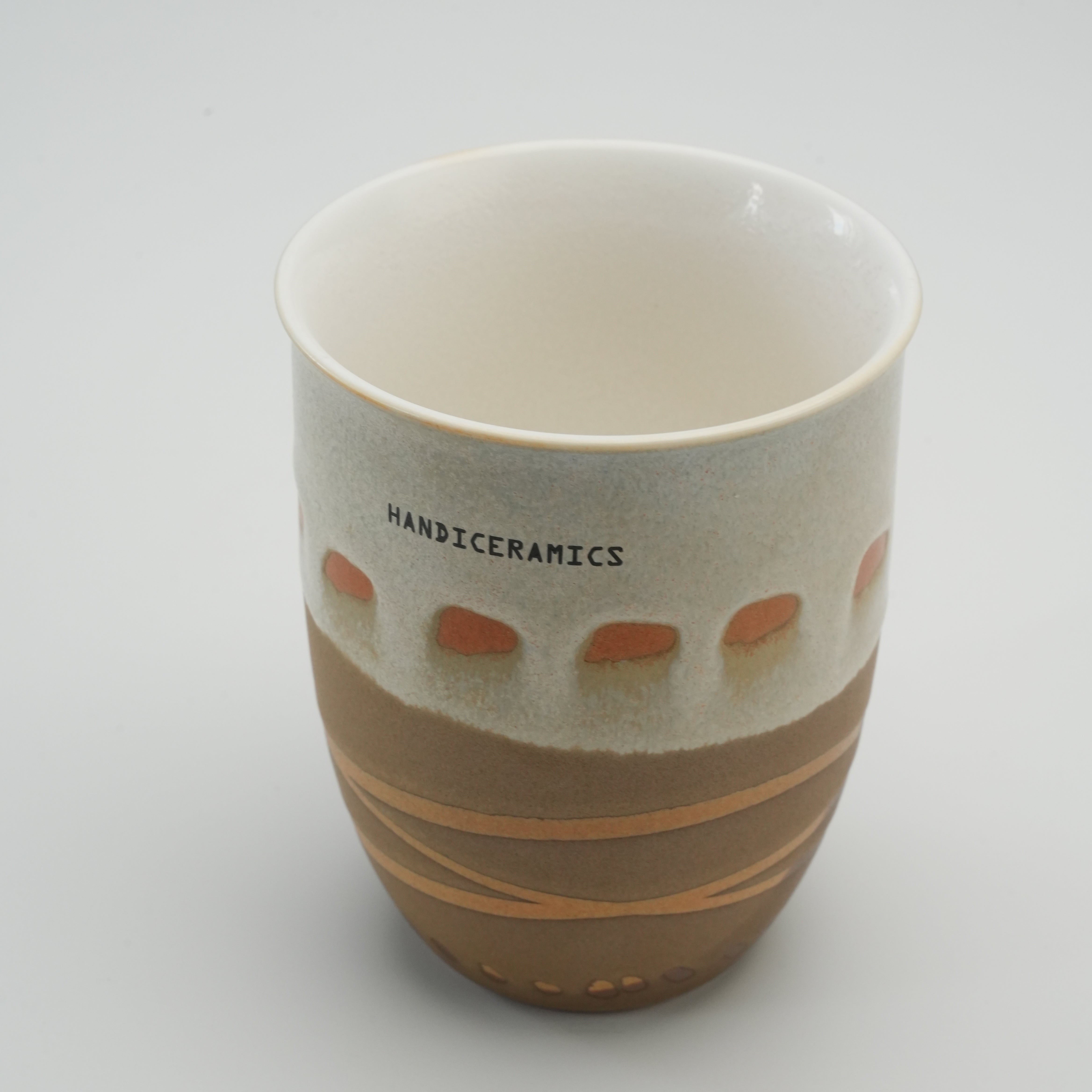 Open view of Handiceramics Travel Cup in mocha, showing white glazed interior and handcrafted ceramic exterior with acorn pattern.