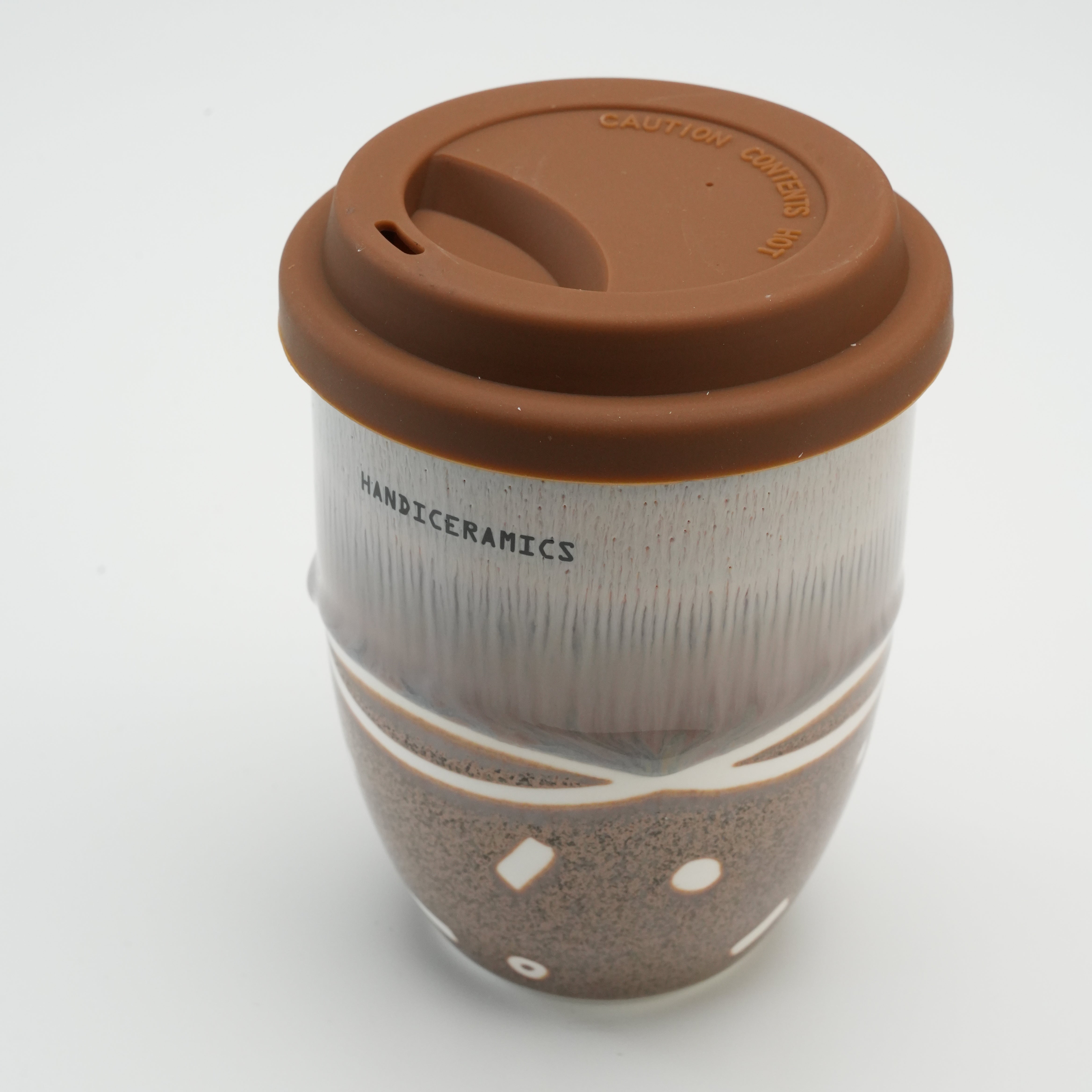 Close-up of Handiceramics Travel Cup with Brown Sugar silicone lid, highlighting textured ceramic surface and secure drinking spout.