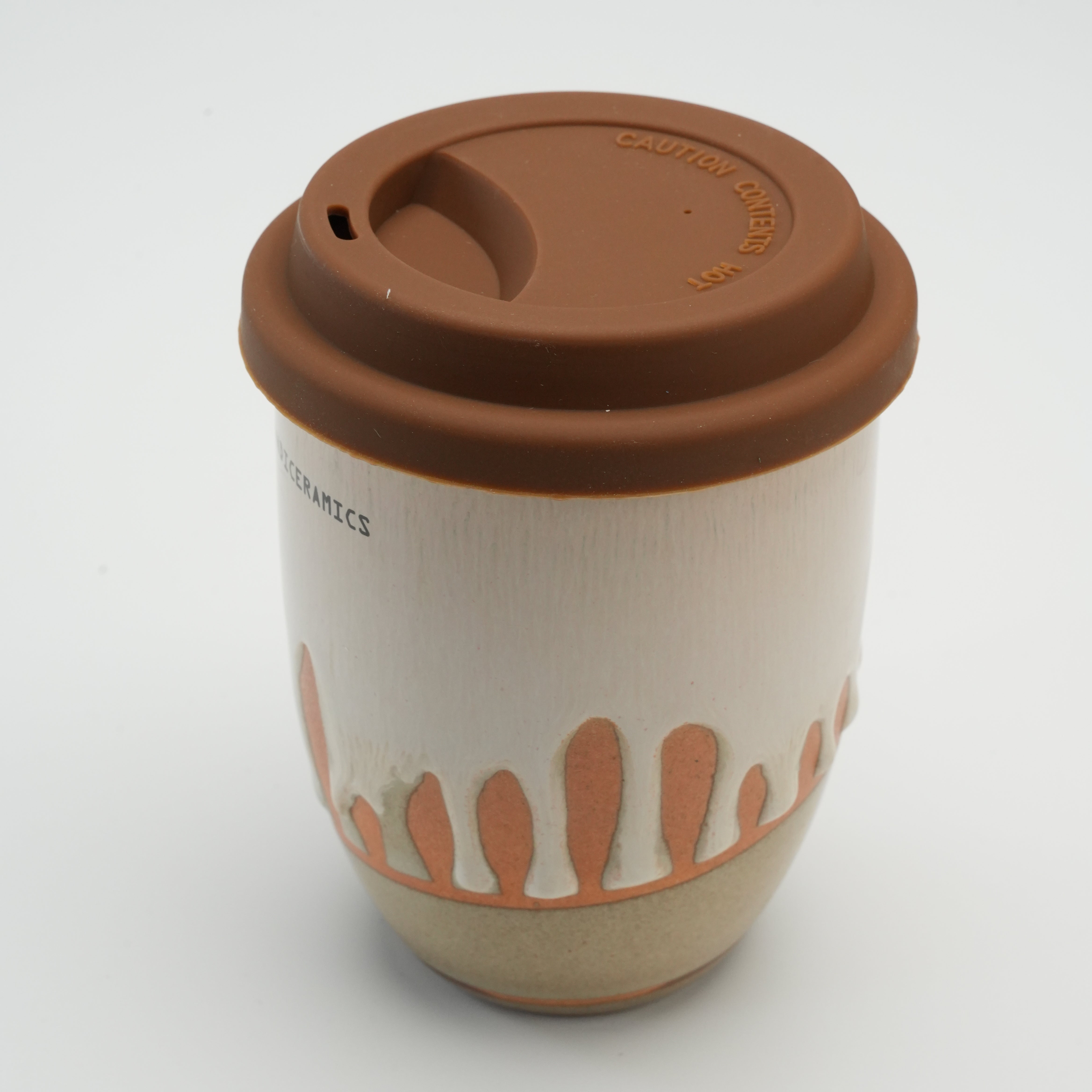 Angled view of Handiceramics Ceramic Coffee Cup with brown lid, highlighting drip glaze design and ergonomic shape for travel use.