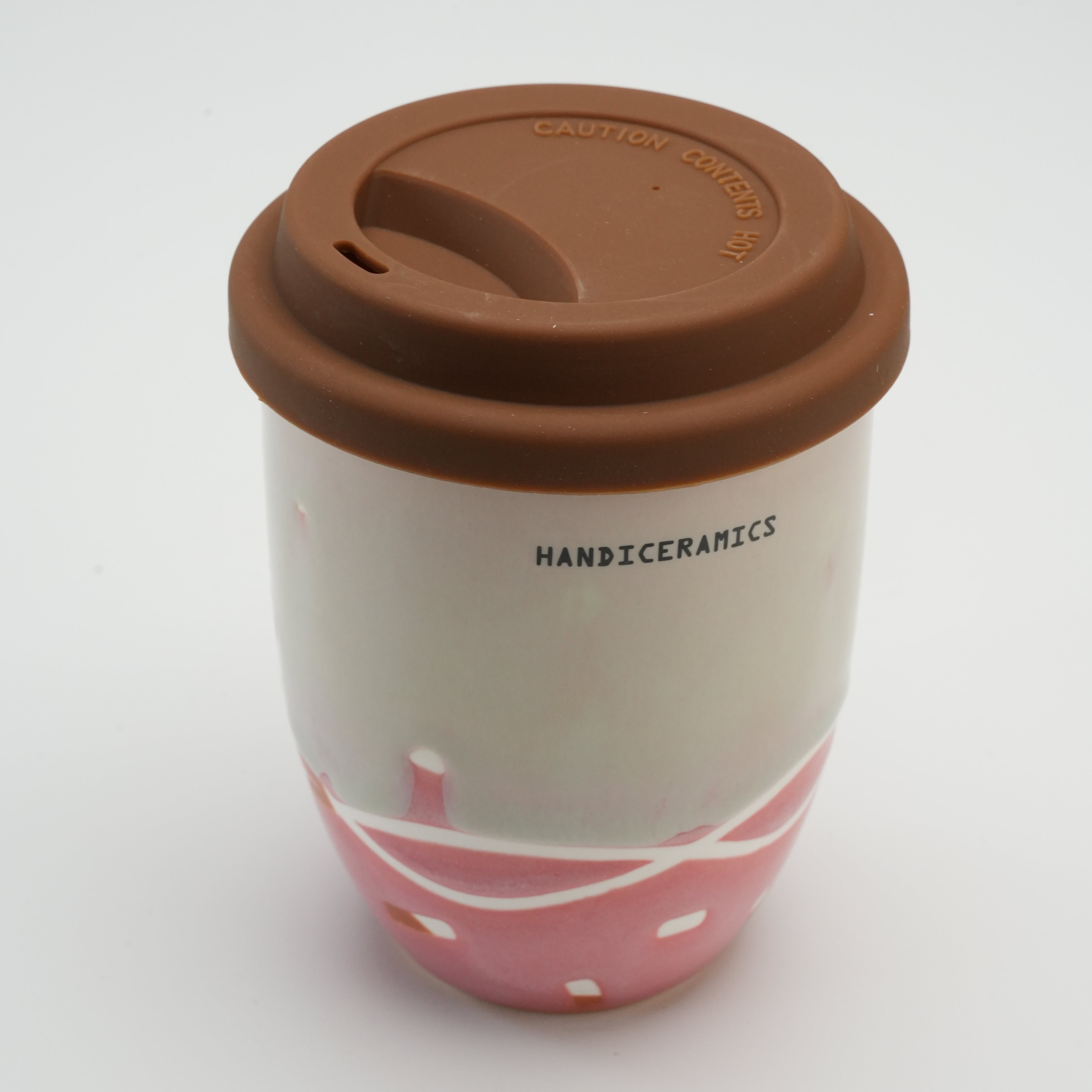 Close-up of Handiceramics ceramic travel cup with brown silicone lid, featuring strawberry pink glaze and modern handmade design.