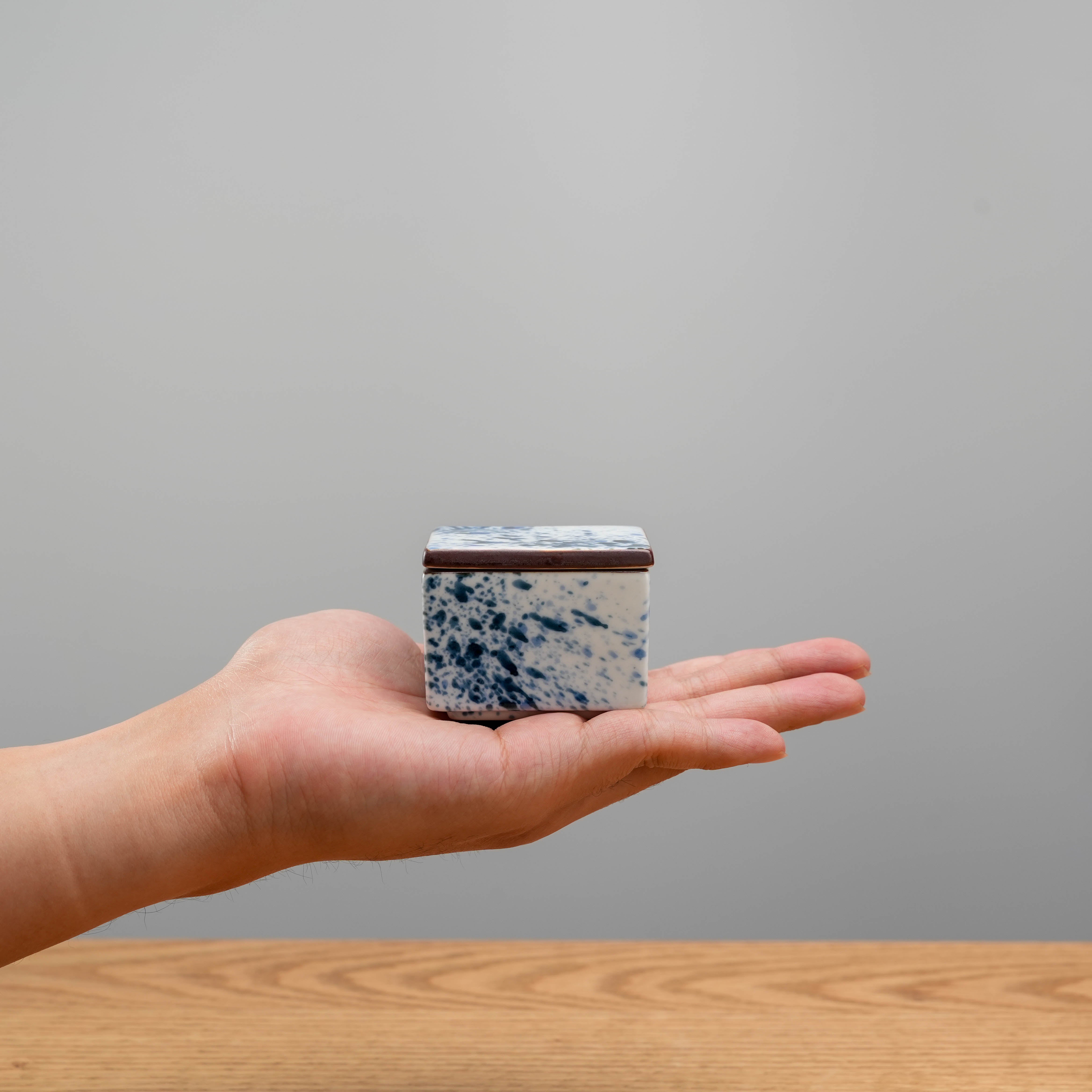 Compact Arita Ware Splash Ink Delicacy Container shown in hand for scale, highlighting its elegant Japanese design and portable size.