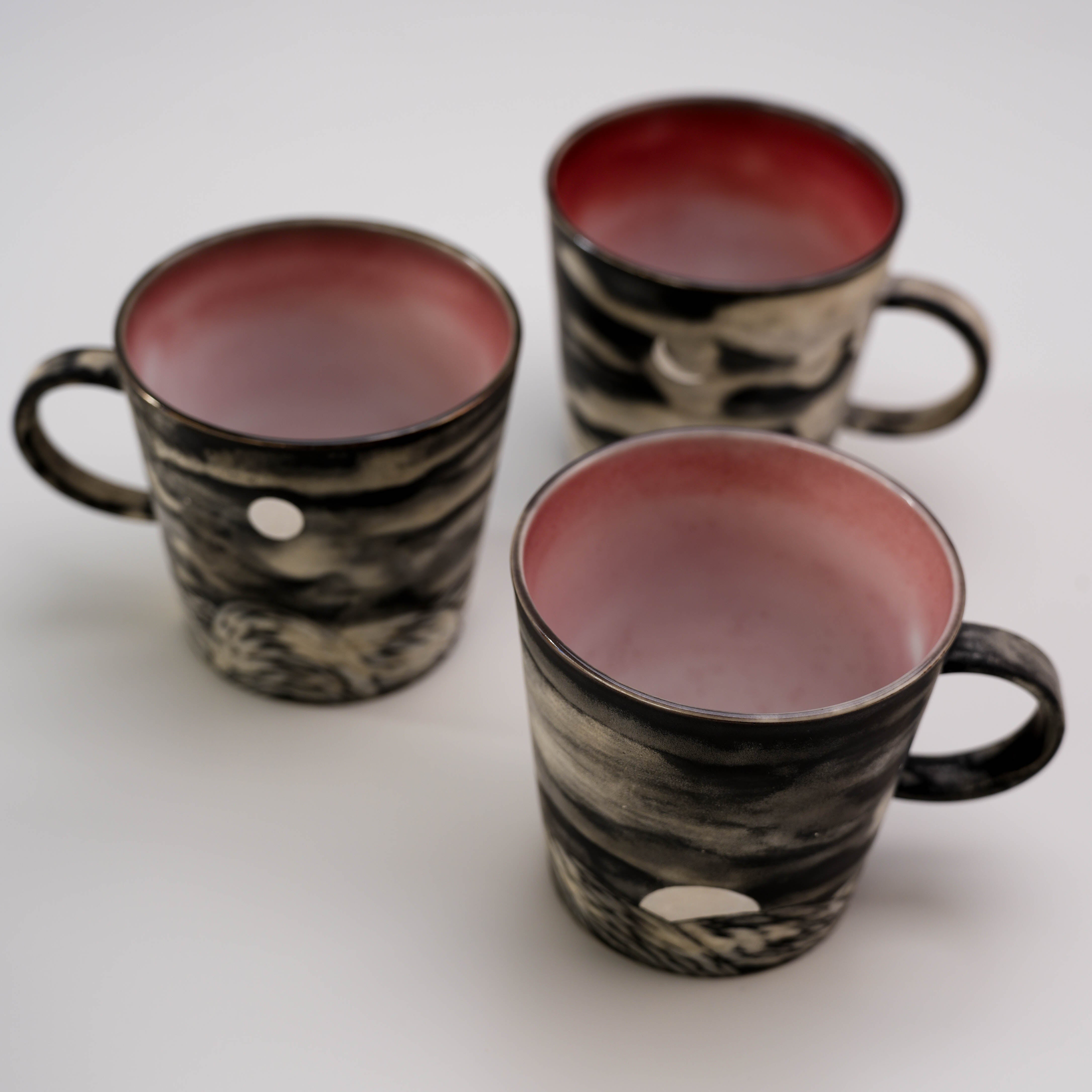 Set of three Evening Moon Mugs with red interiors and silver glazed moonrise designs, perfect for artistic kitchen and dining collections.