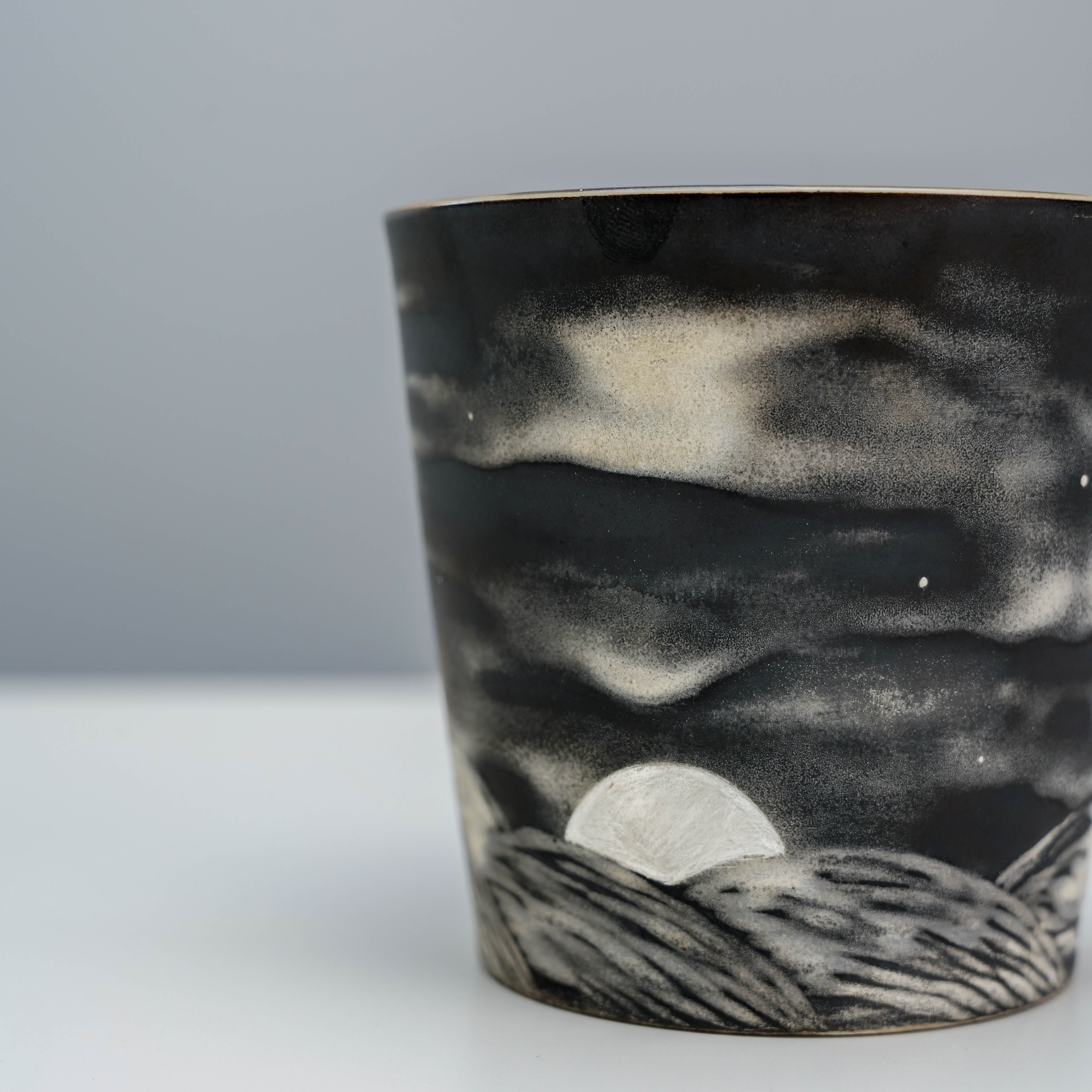 Close-up of Evening Moon Mug's hand-carved moon and hills design with silver glaze, highlighting craftsmanship in ceramic drinkware.