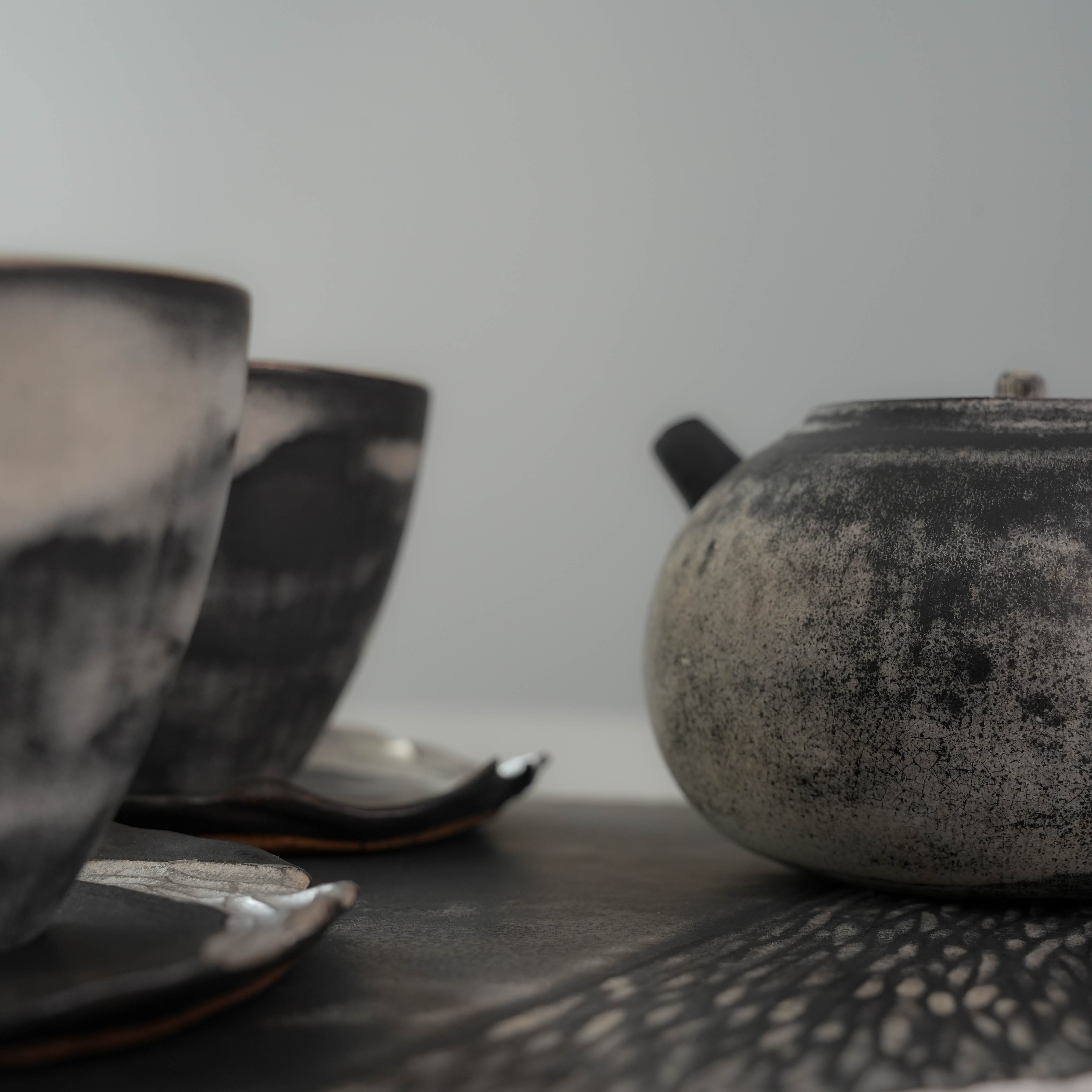 Side view of Lonesome Studio Gushan Tea Set teapot and cups, highlighting the rustic black and white glaze and artisanal finish.