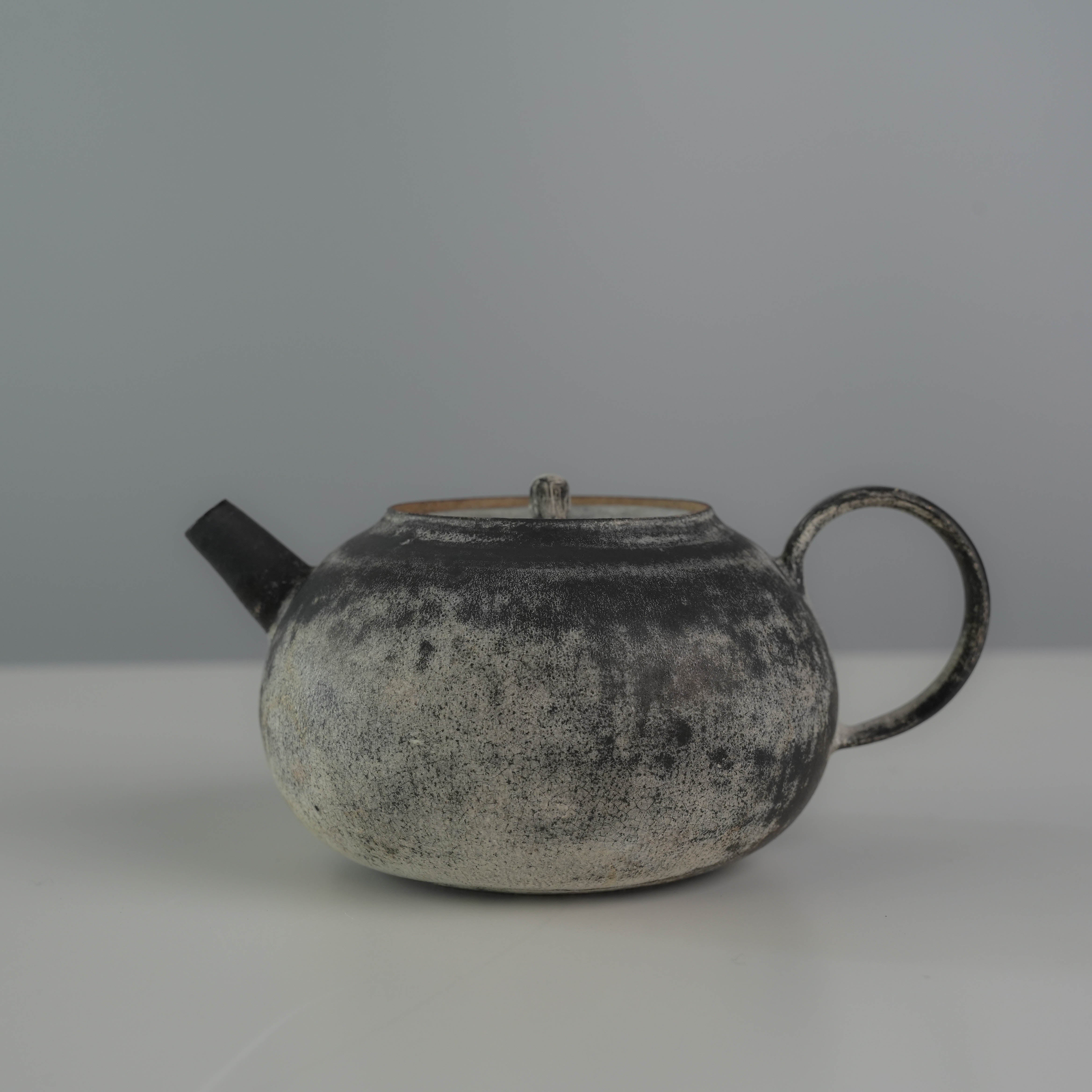 Side profile of the Lonesome Studio Gushan Tea Set teapot with a rounded body and black-silver gradient glaze.