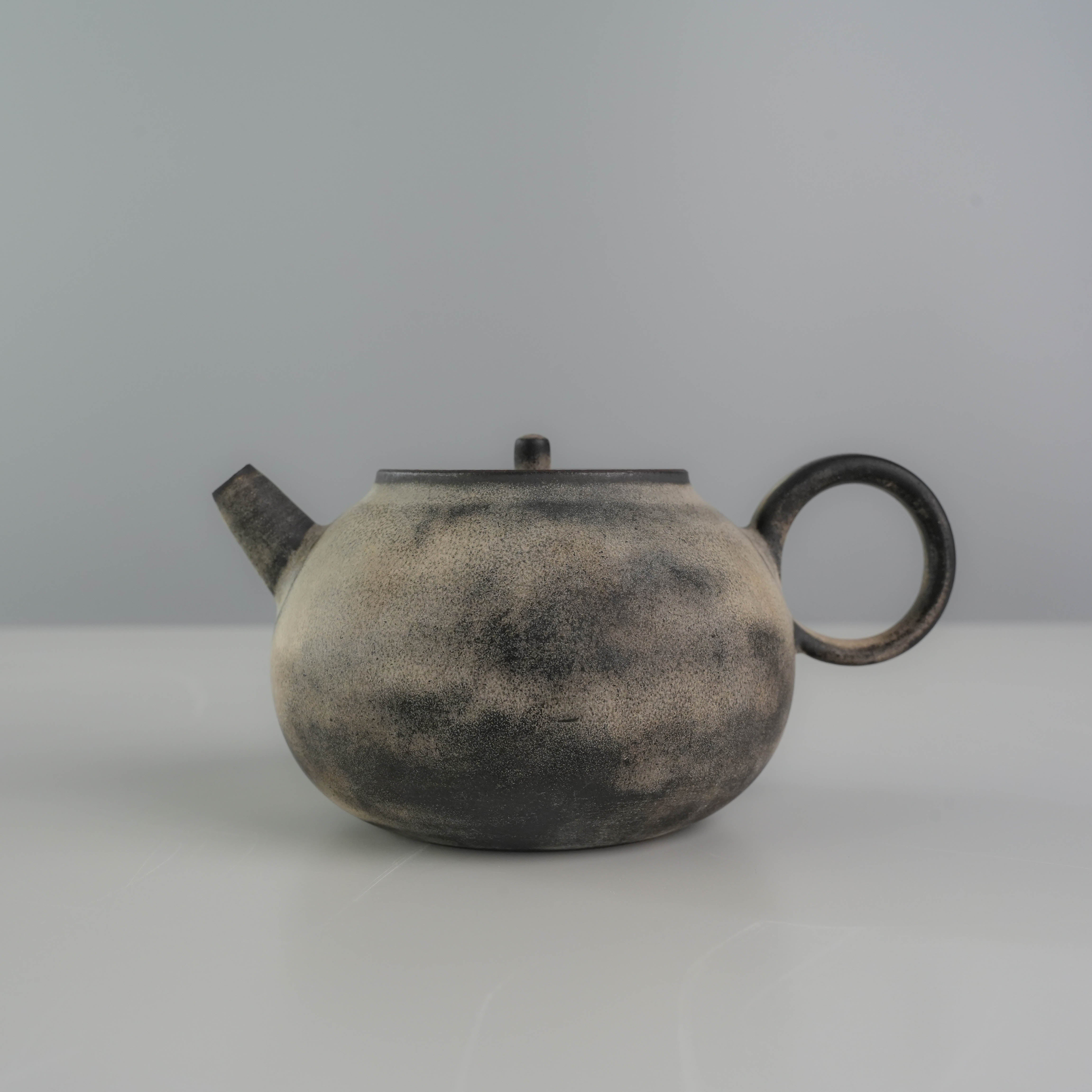 Side view of Lonesome Studio Gushan Tea Set teapot with a rounded body and loop handle, finished in silver glaze.