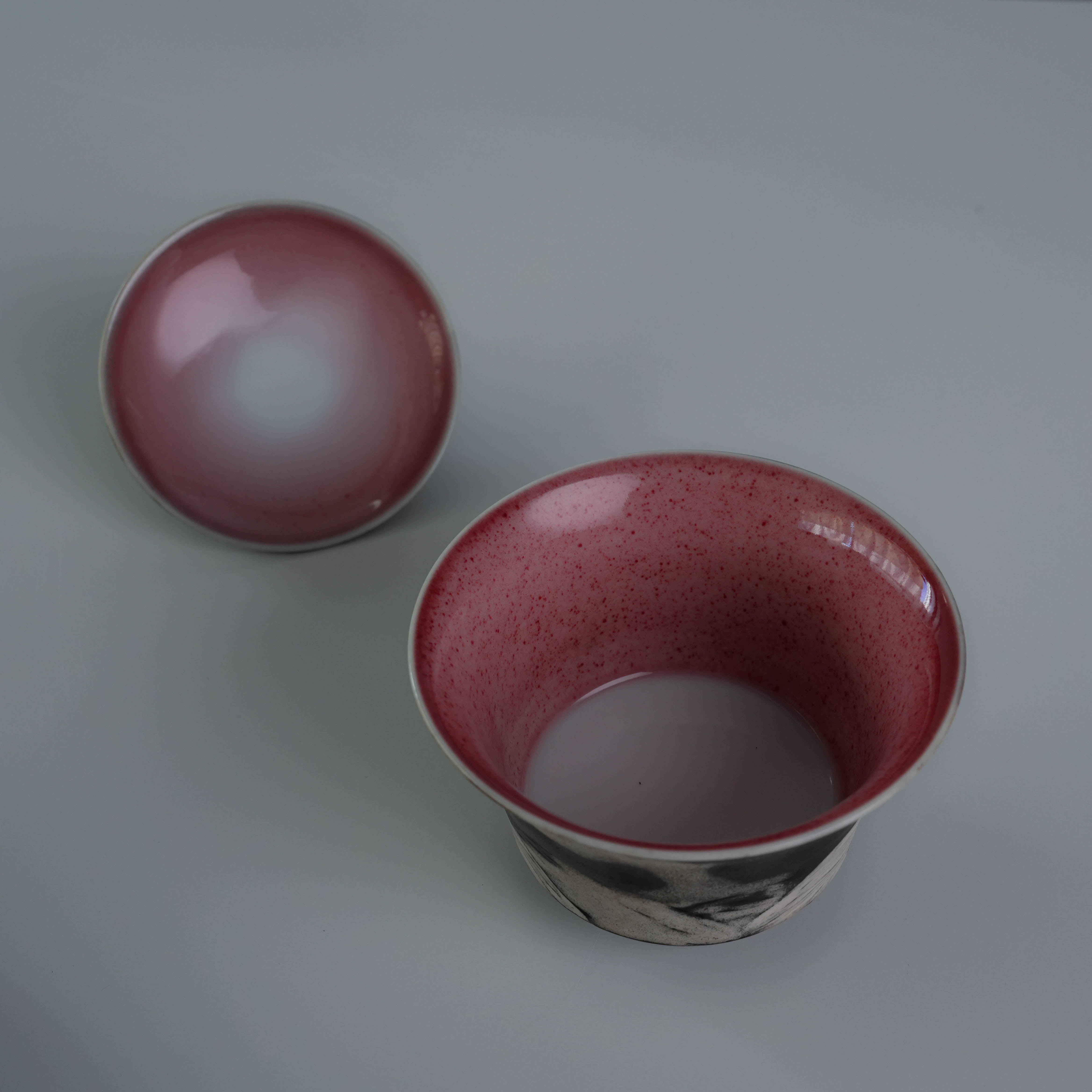 Close-up of Lonesome Studio Qushui tea cups with red glazed interiors and silver-glazed exteriors, part of handmade Gongfu Cha tea set.