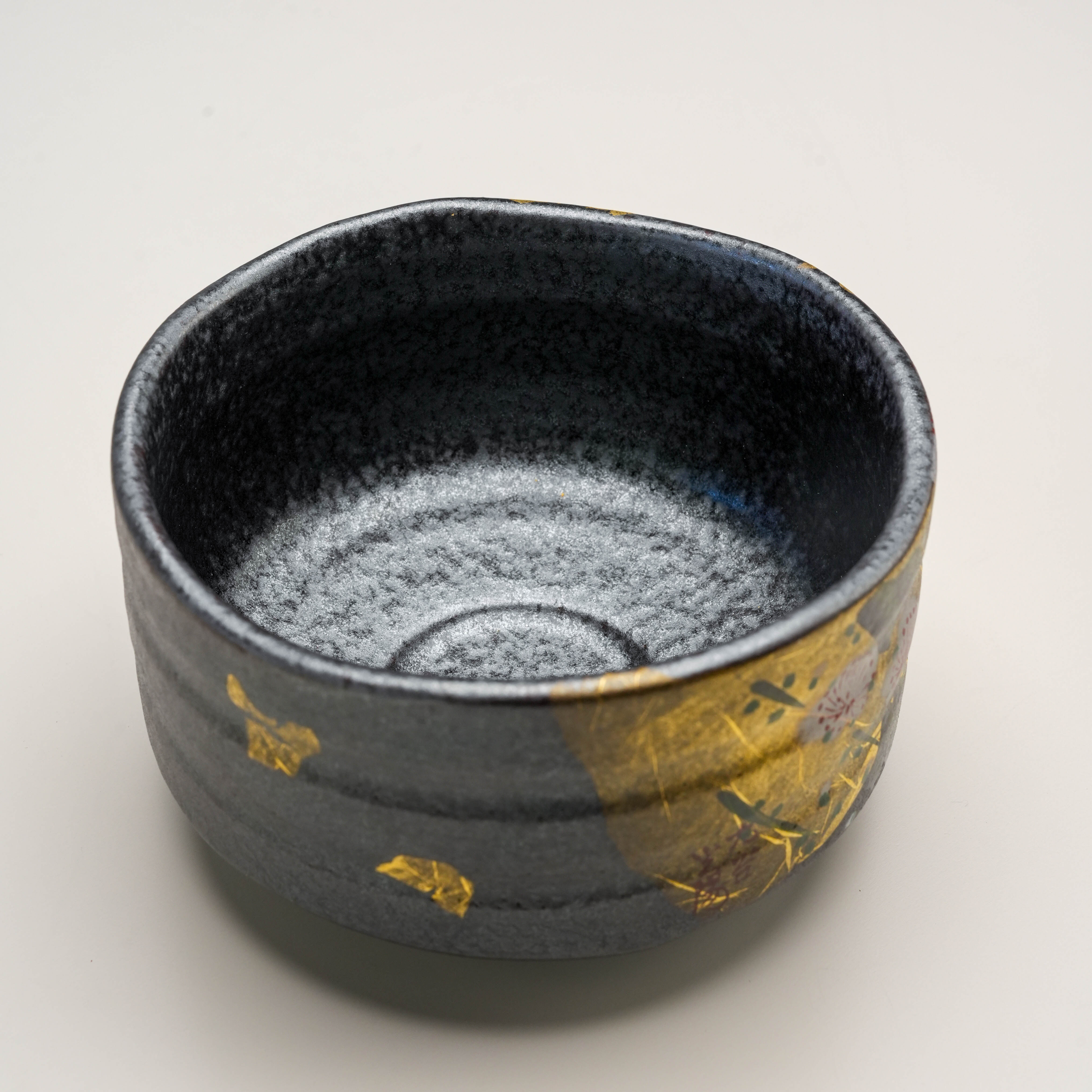 Interior view of Kutani Ware Matcha Bowl featuring a textured black glaze and partial gold leaf plum blossom detailing on the rim.