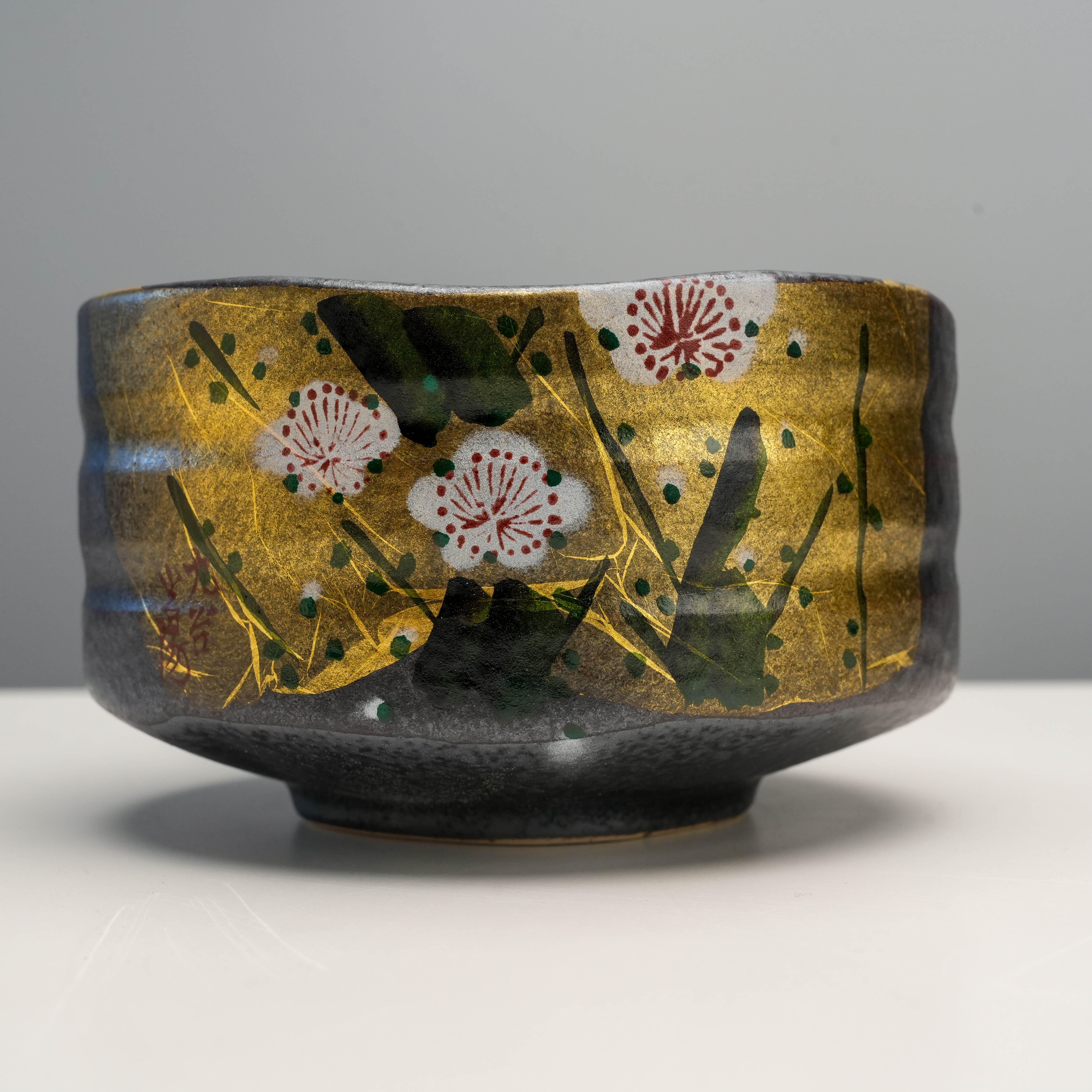 Close-up of Kutani Ware Matcha Bowl highlighting intricate plum blossom artwork and shimmering gold leaf accents on a dark ceramic base.