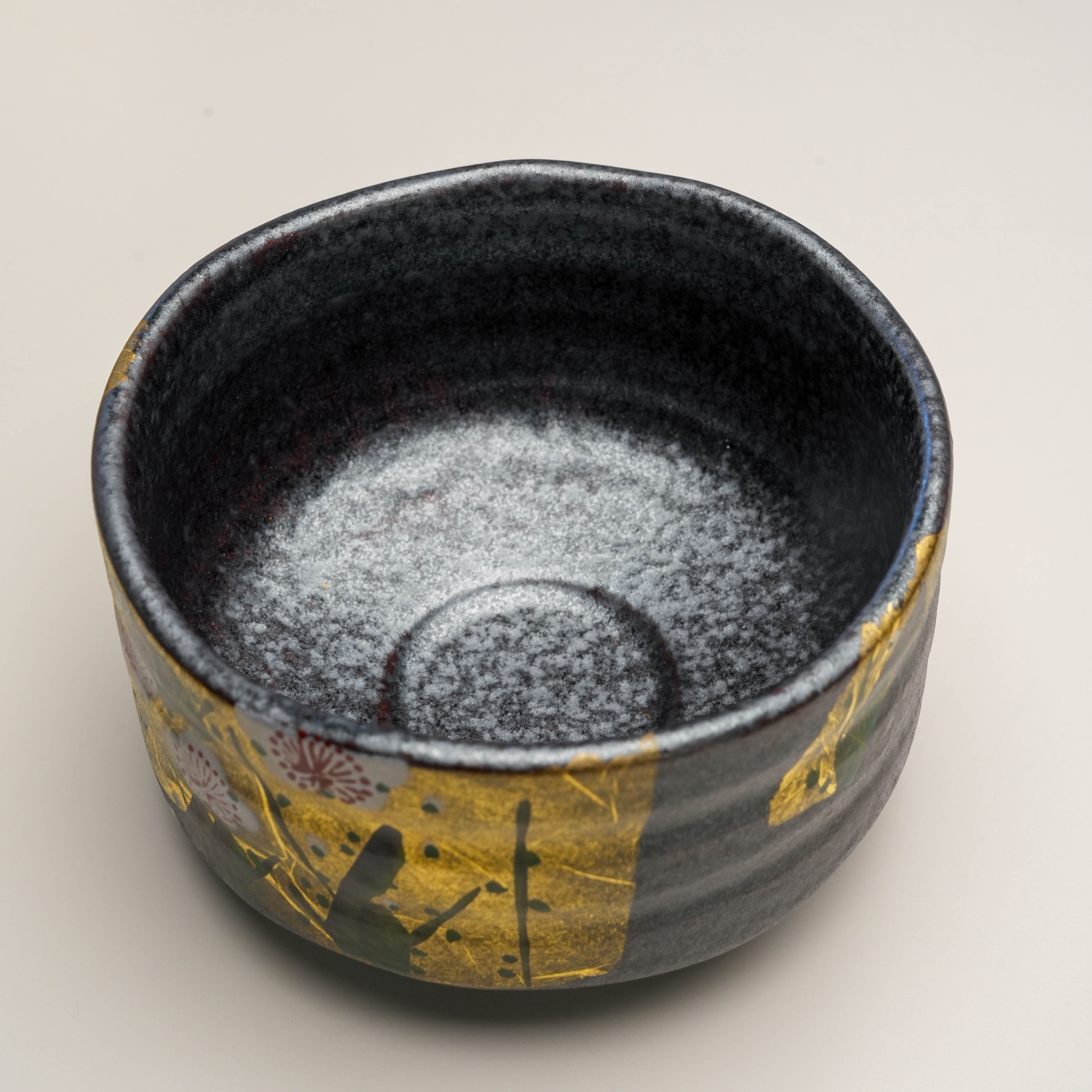 Top view of Kutani Ware Plum Blossom Matcha Bowl with speckled black glaze and elegant gold leaf floral design on the outer rim.