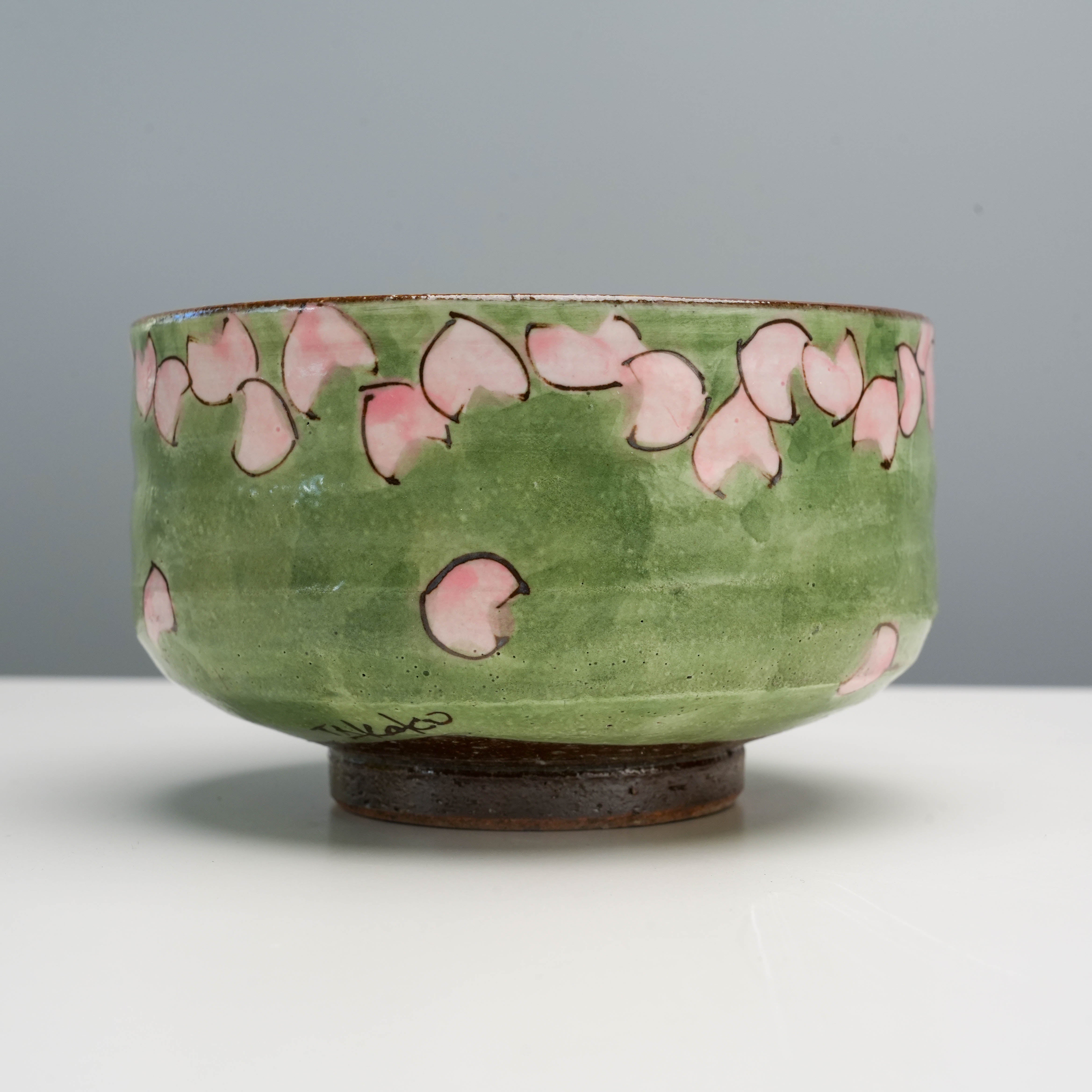 Close-up of Kutani Ware Matcha Bowl featuring hand-painted cherry blossom petals on a green background, showcasing artisanal craftsmanship.