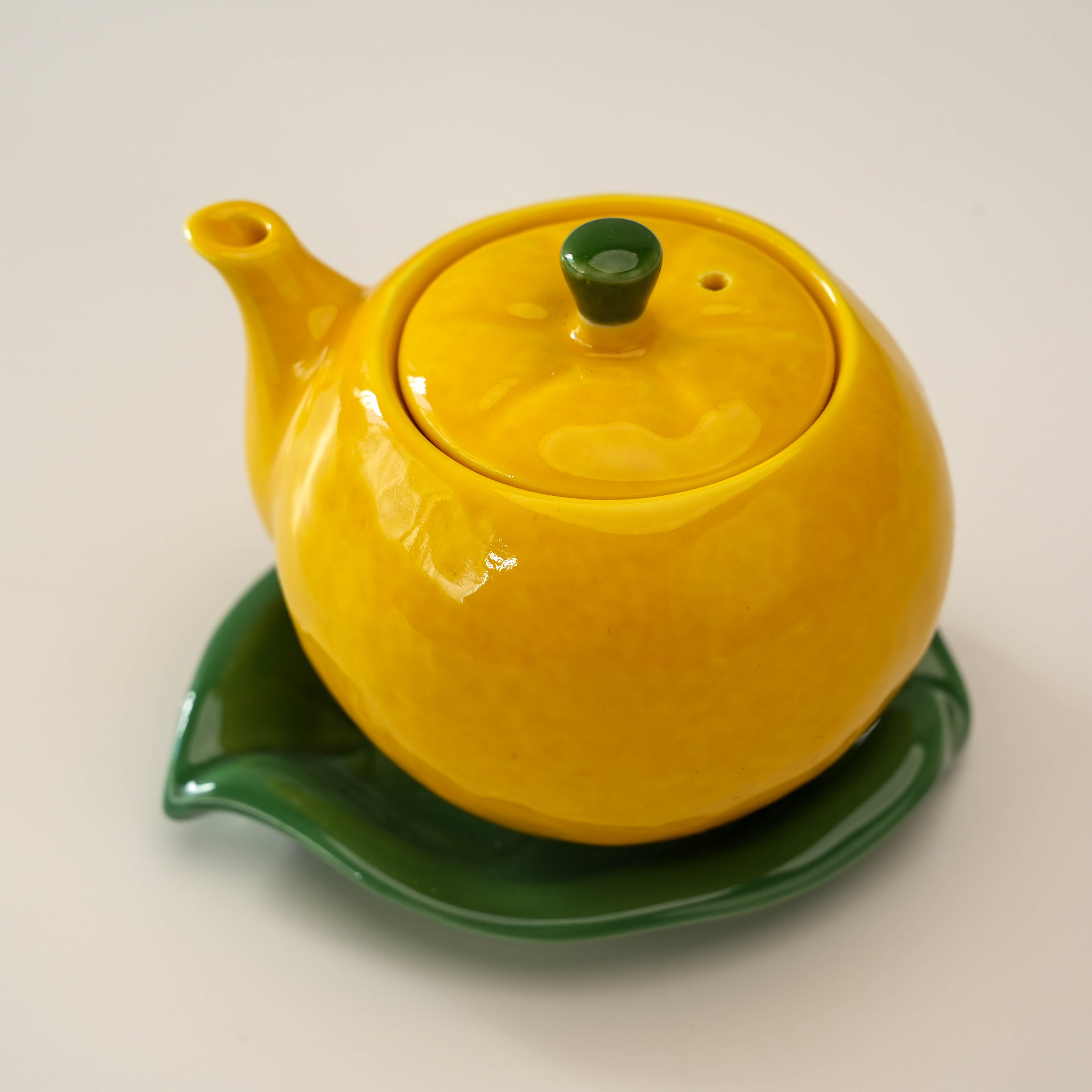 Japanese porcelain Arita Ware Yuzu Soy Sauce Dispenser with lid and spout, resting on a green leaf-shaped saucer.