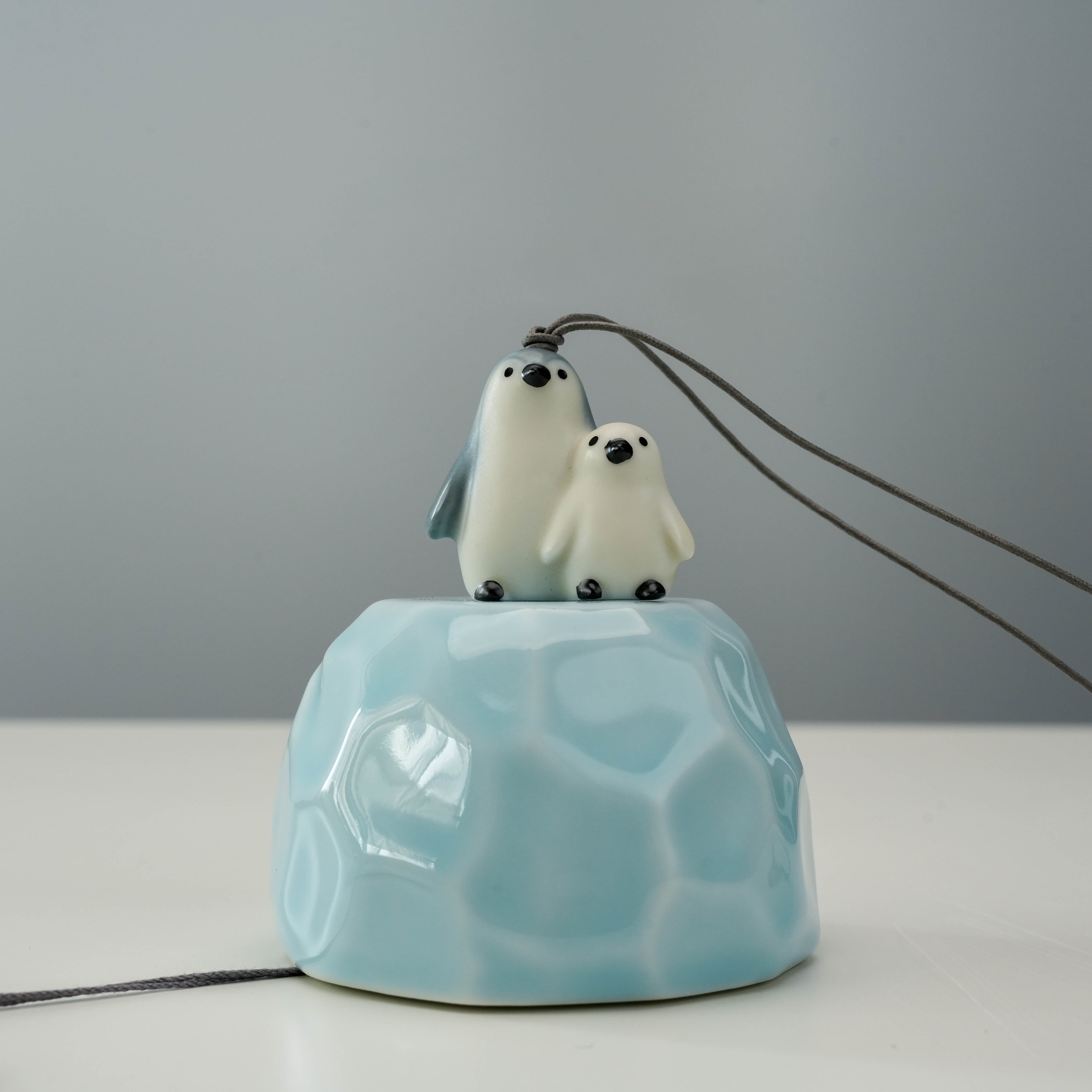 Close-up of Penguin Wind Chime showing detailed ceramic figures of a parent and baby penguin on a glossy blue bell, perfect for indoor decor.
