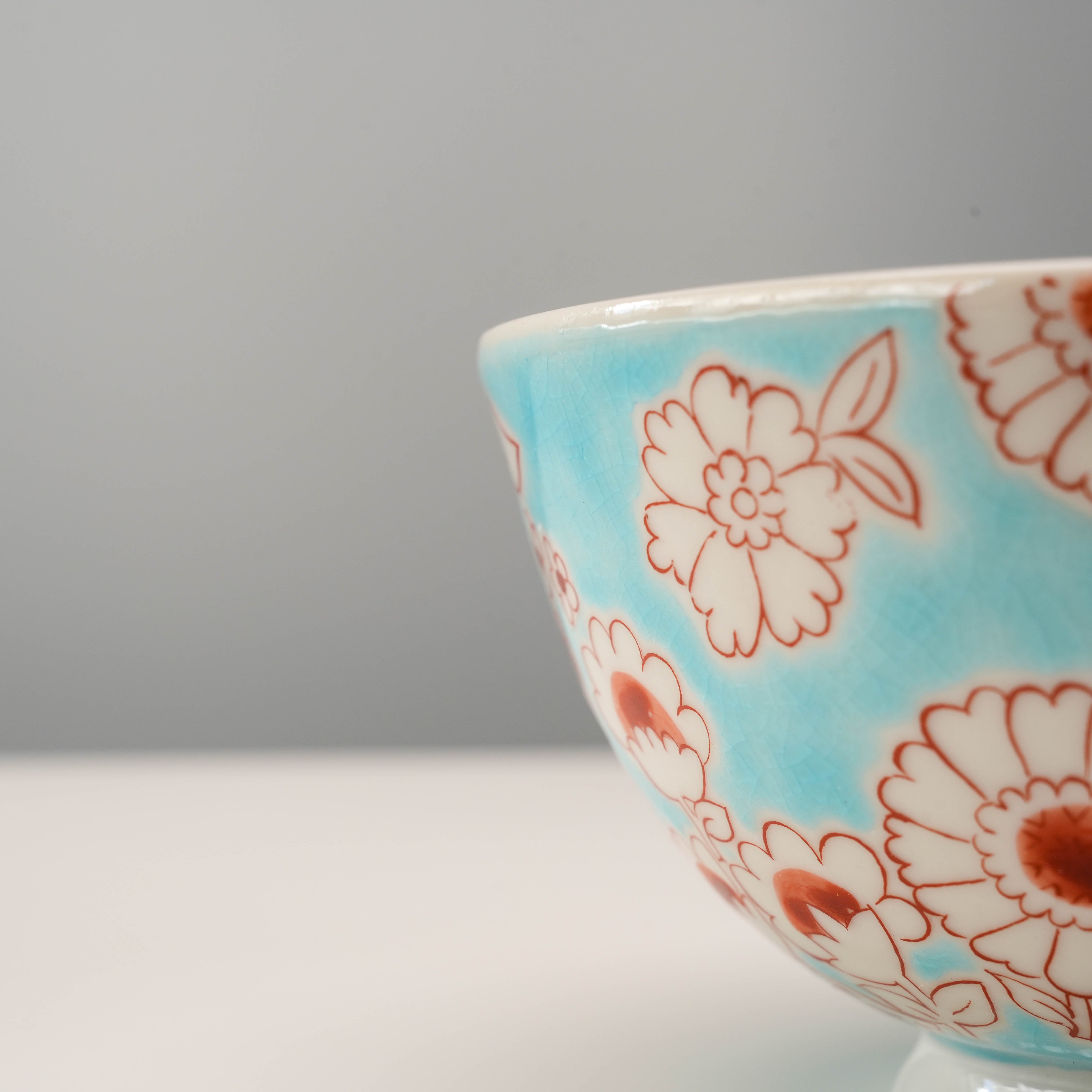 Detailed side view of Flower Shower Kutani Rice Bowl highlighting intricate red floral prints on crackle-glazed blue porcelain surface.