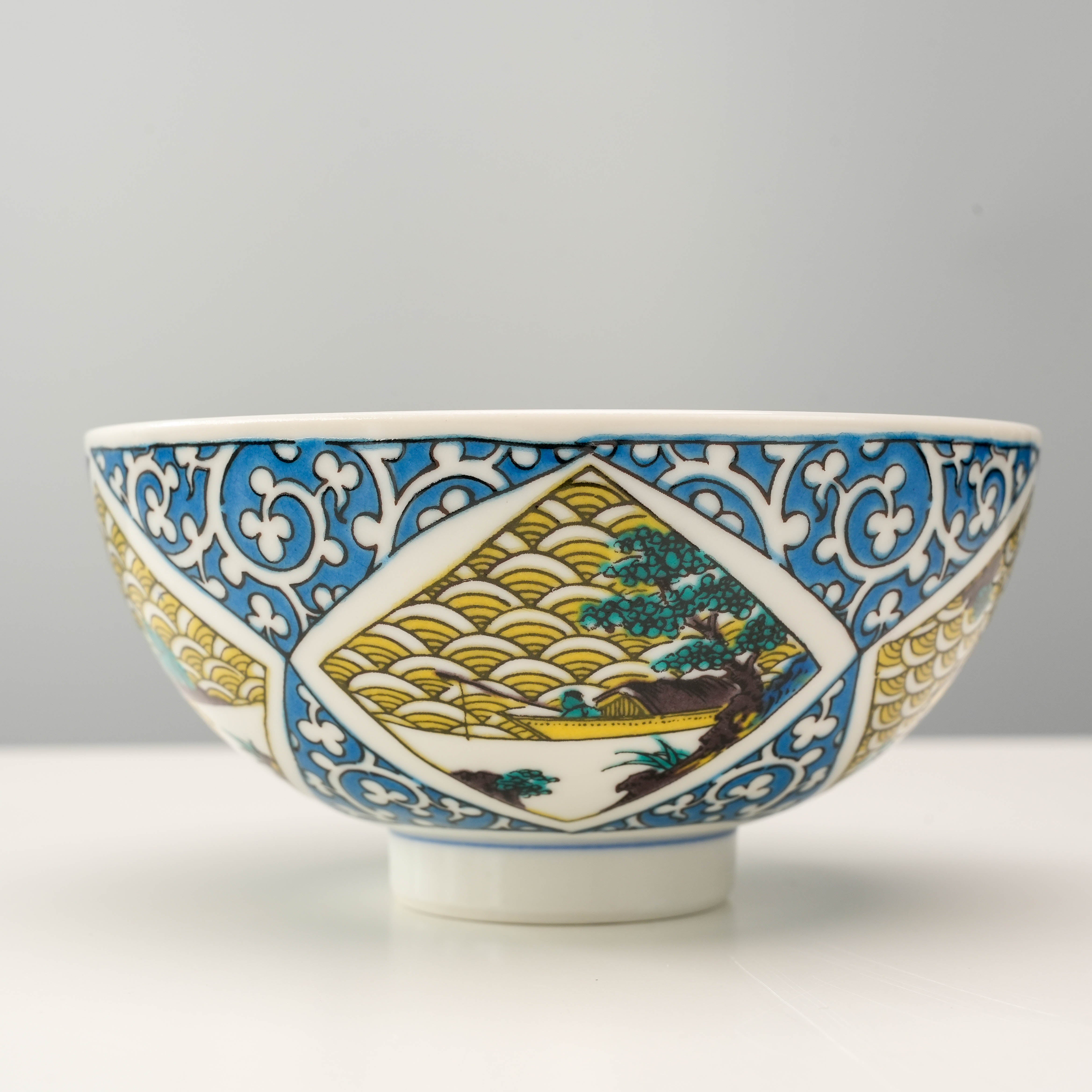 Japanese Kutani Ware Rice Bowl with blue arabesque border and serene landscape illustration, blending art and function in dinnerware.