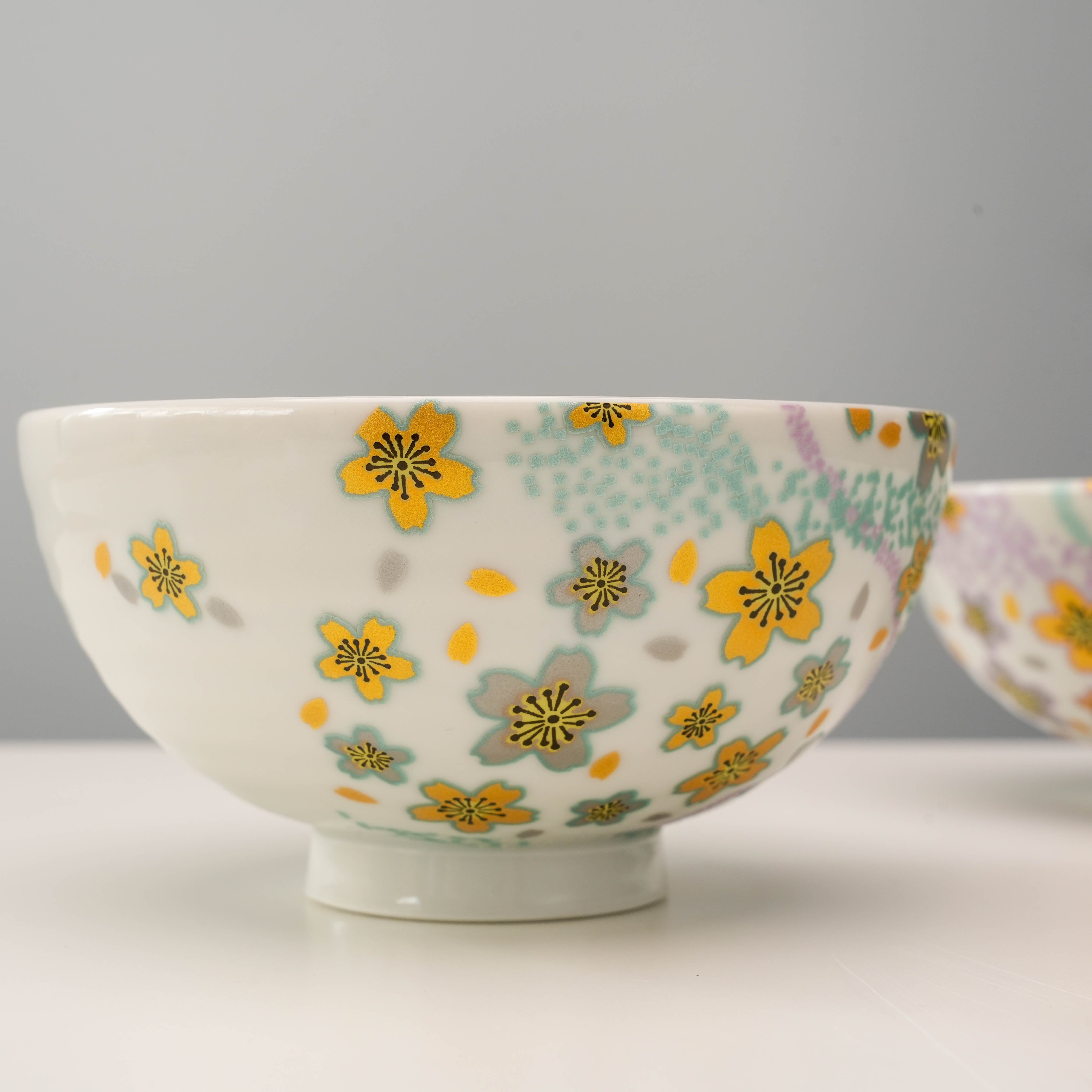Close-up of Kutani Ware rice bowl with yellow Kyokusui flowers and green accents, highlighting intricate craftsmanship and pastel charm.