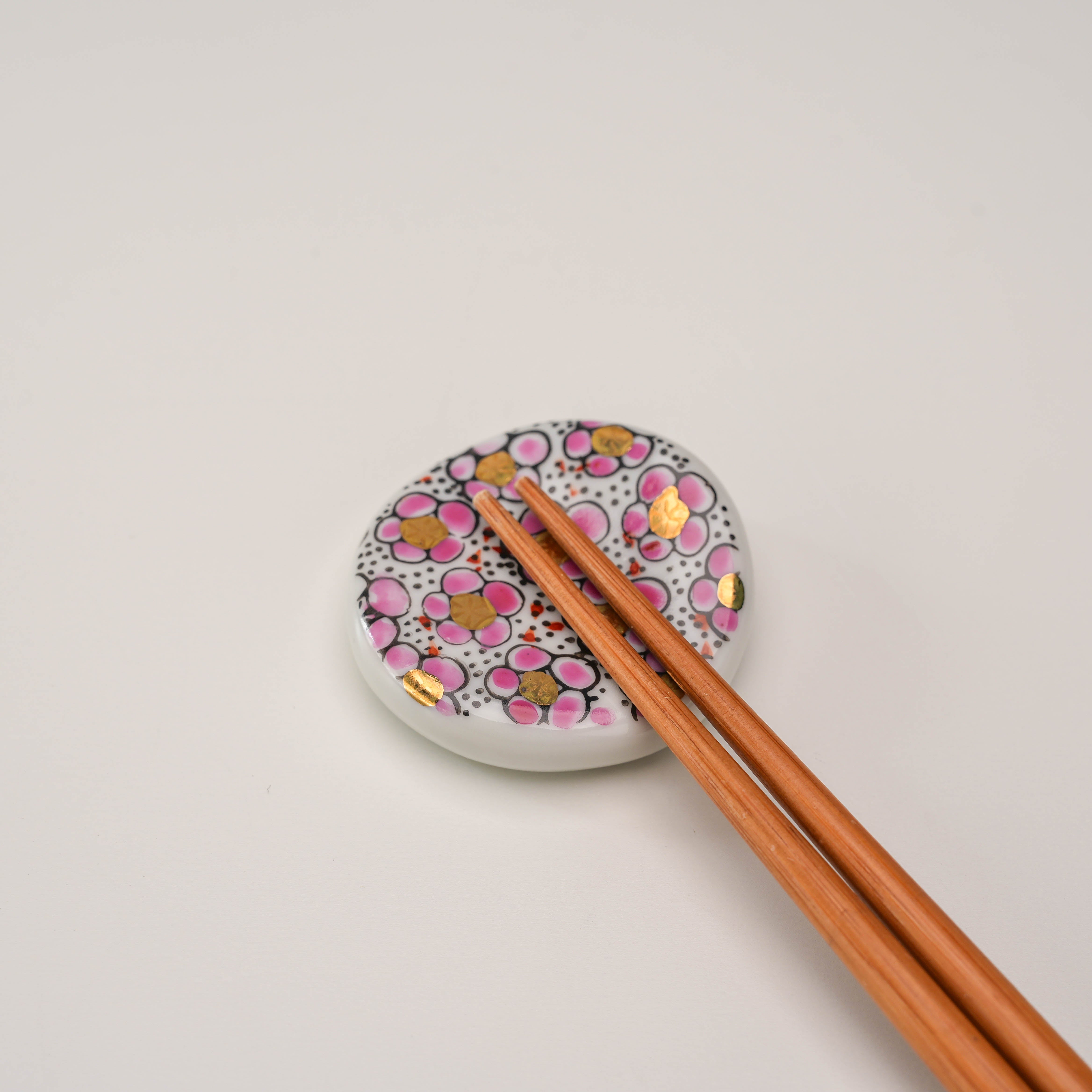 Pink Kutani Ware Plum Blossom Chopstick Rest in use with wooden chopsticks, showcasing its functional and decorative appeal.