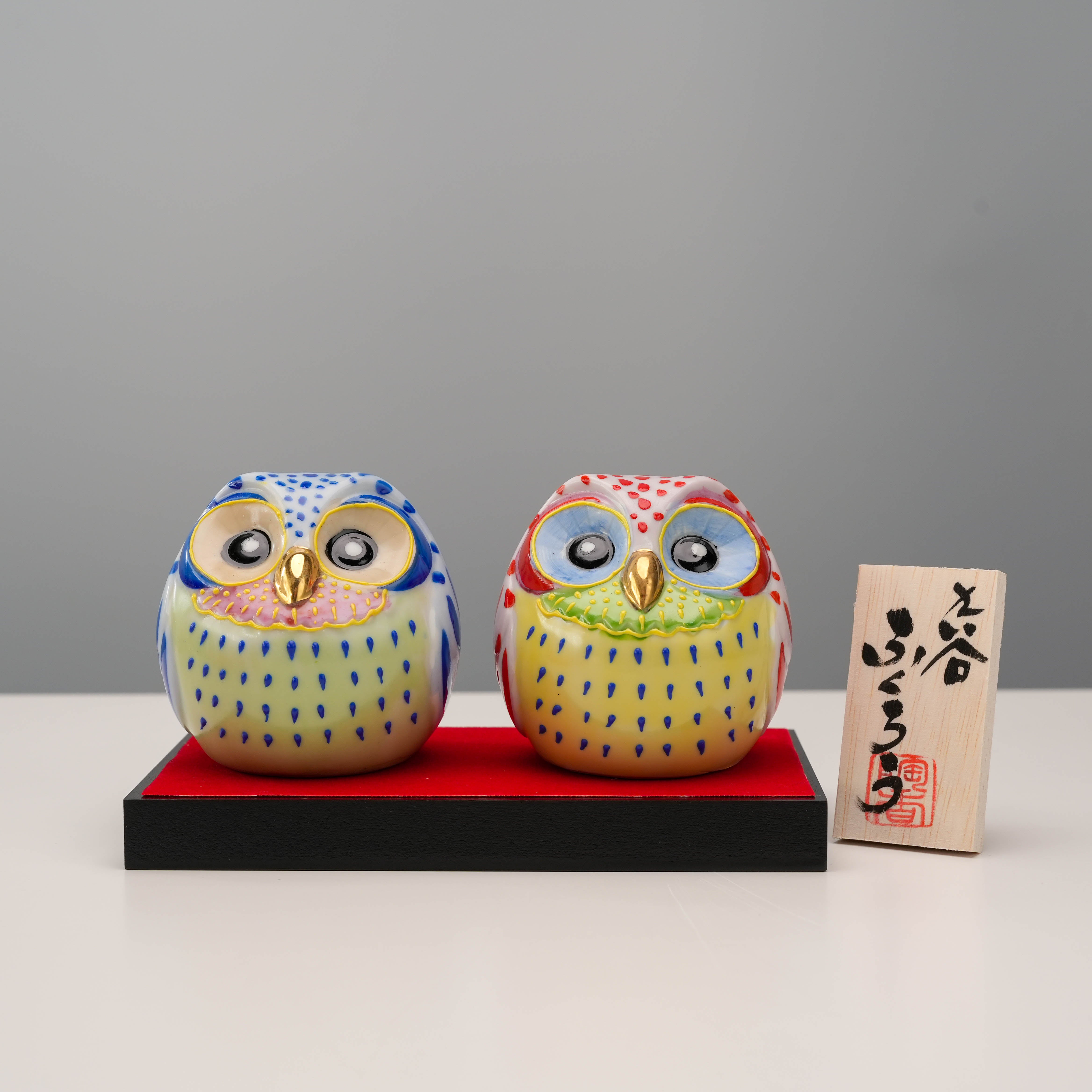 Kutani Owl Pair - Lucky Ornament on red base with Japanese name plaque. Colorful ceramic owls bring charm and protection to any space.