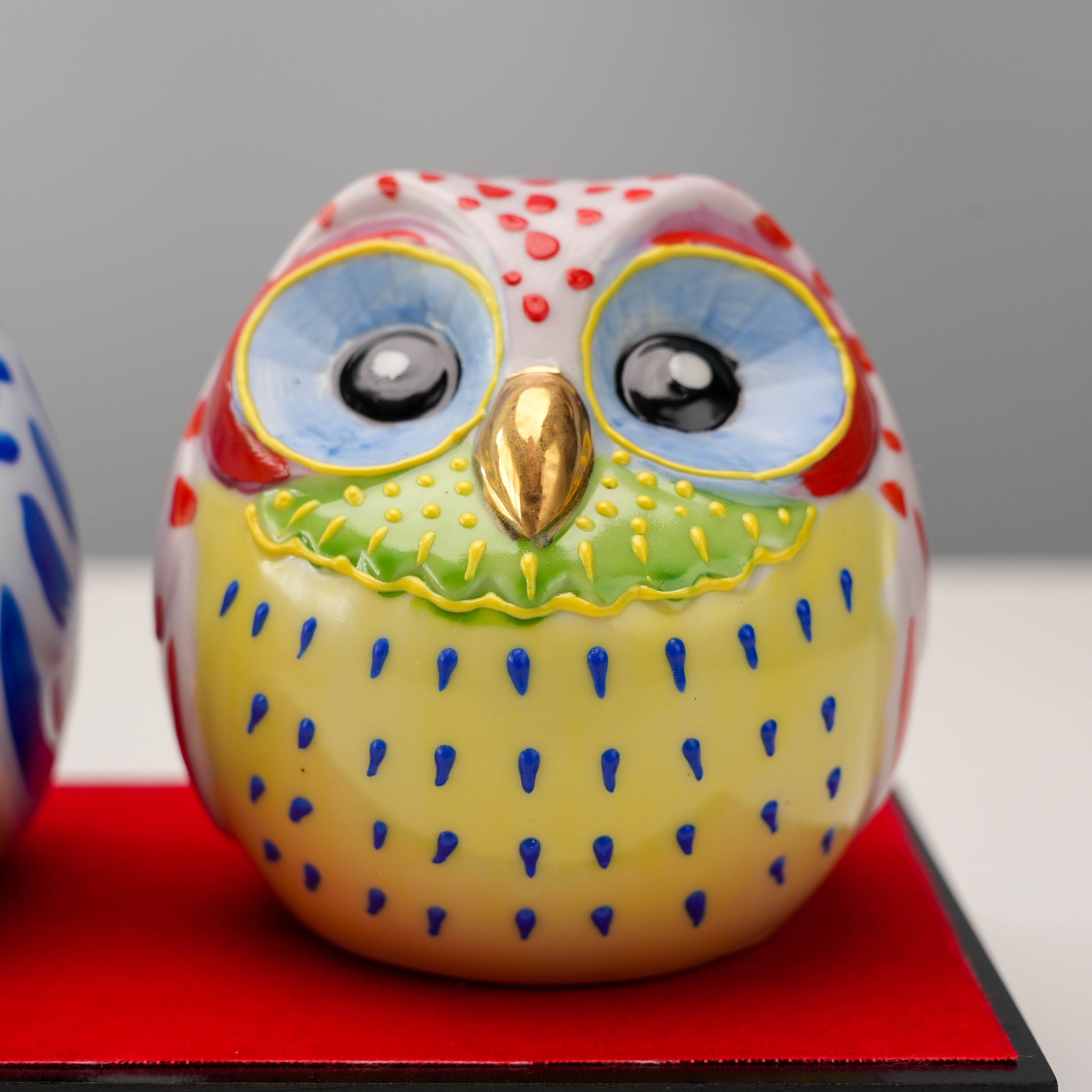 Close-up of red Kutani owl figurine with blue eyes and golden beak. A cheerful and symbolic home decor piece for good luck and wisdom.