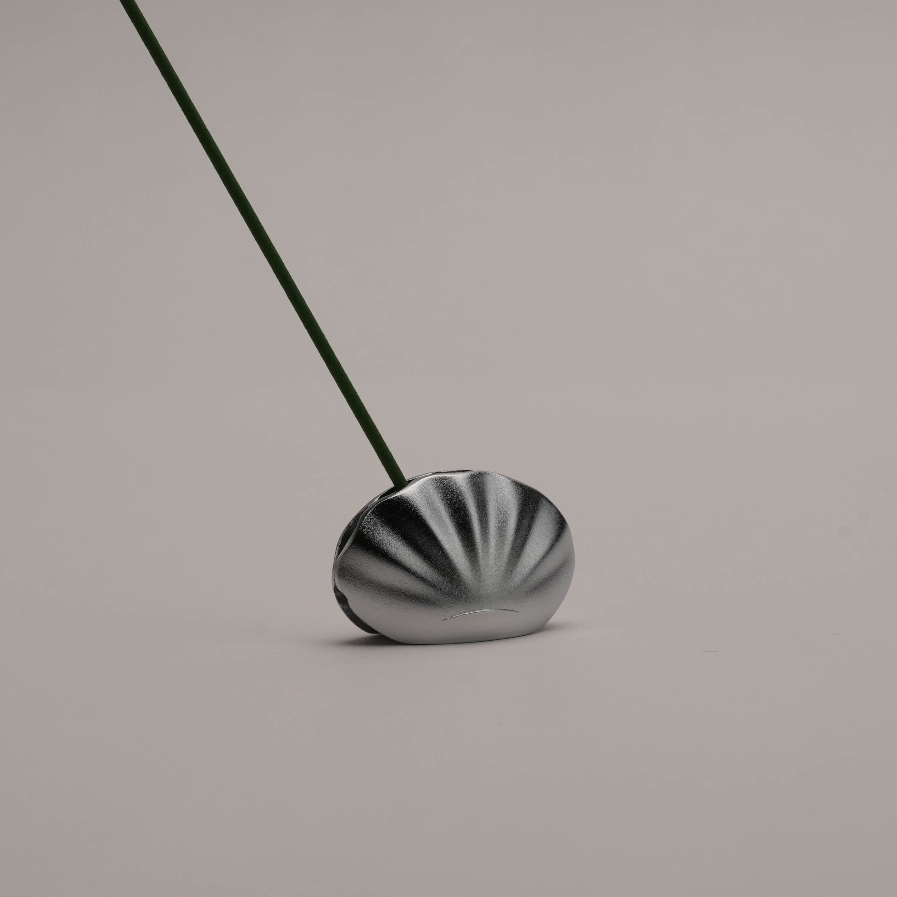 Close-up of Kolip Shell Incense Holder by Shoyeido in matte silver, showcasing its secure clamshell design with incense stick inserted.