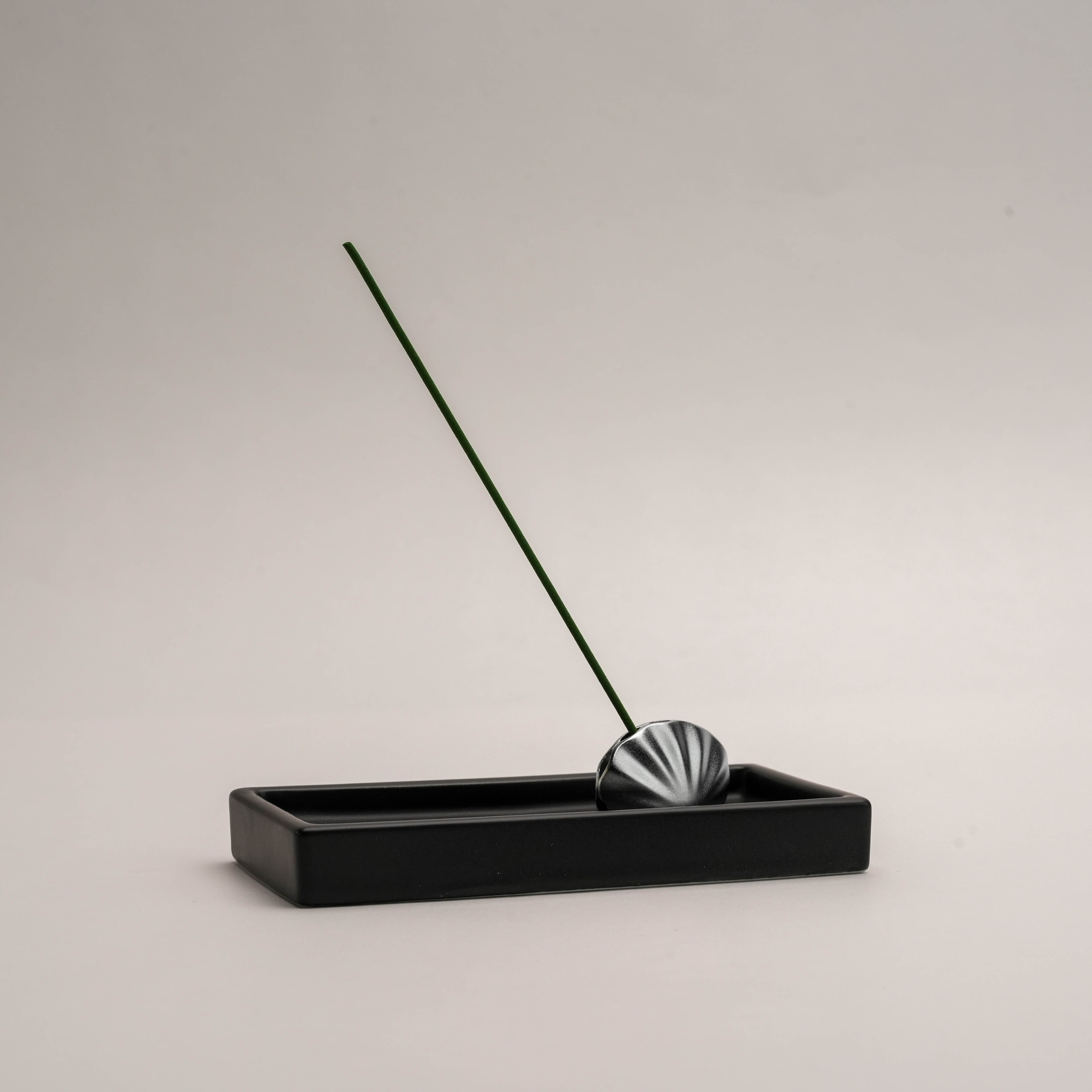 Shoyeido Kolip Shell incense holder and tray set in black, featuring a minimalist shell-shaped holder securely supporting a green incense stick.