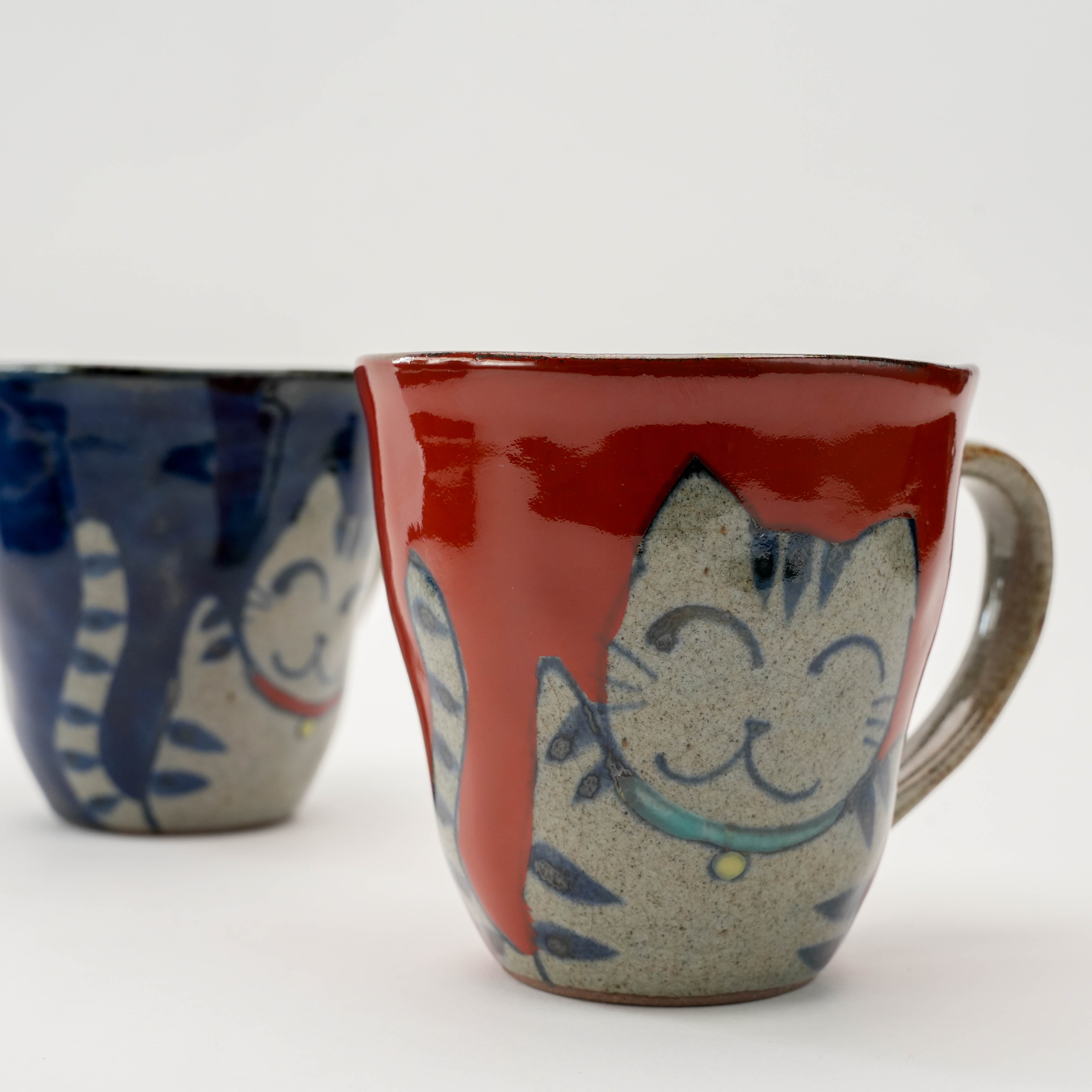 Red Arita Ware Lucky Cat Mug with smiling cat illustration, part of a Japanese-inspired ceramic pair for cheerful kitchen aesthetics.