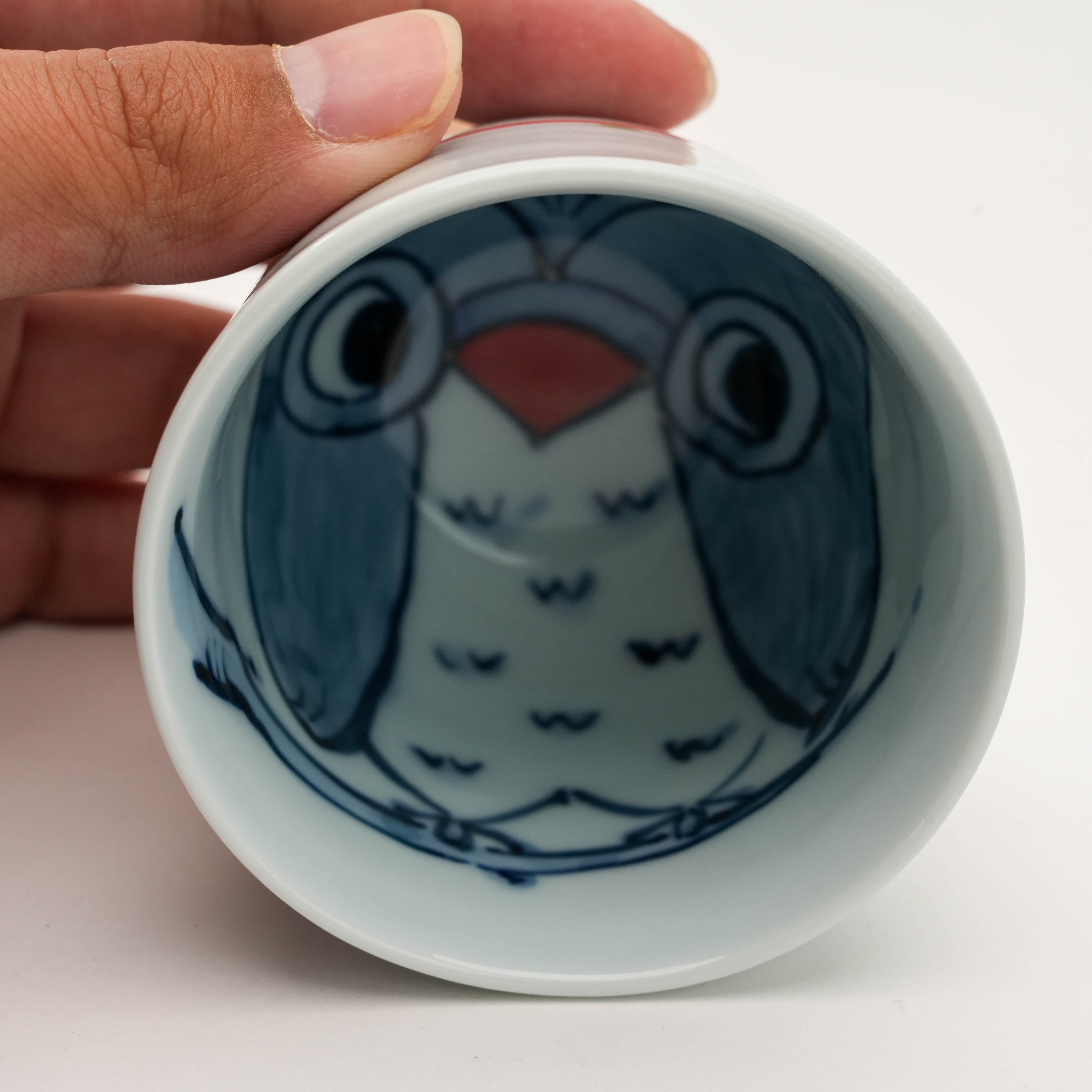 Hand holding Arita Ware Teacup with red owl design inside. Playful Japanese porcelain mug for tea lovers.